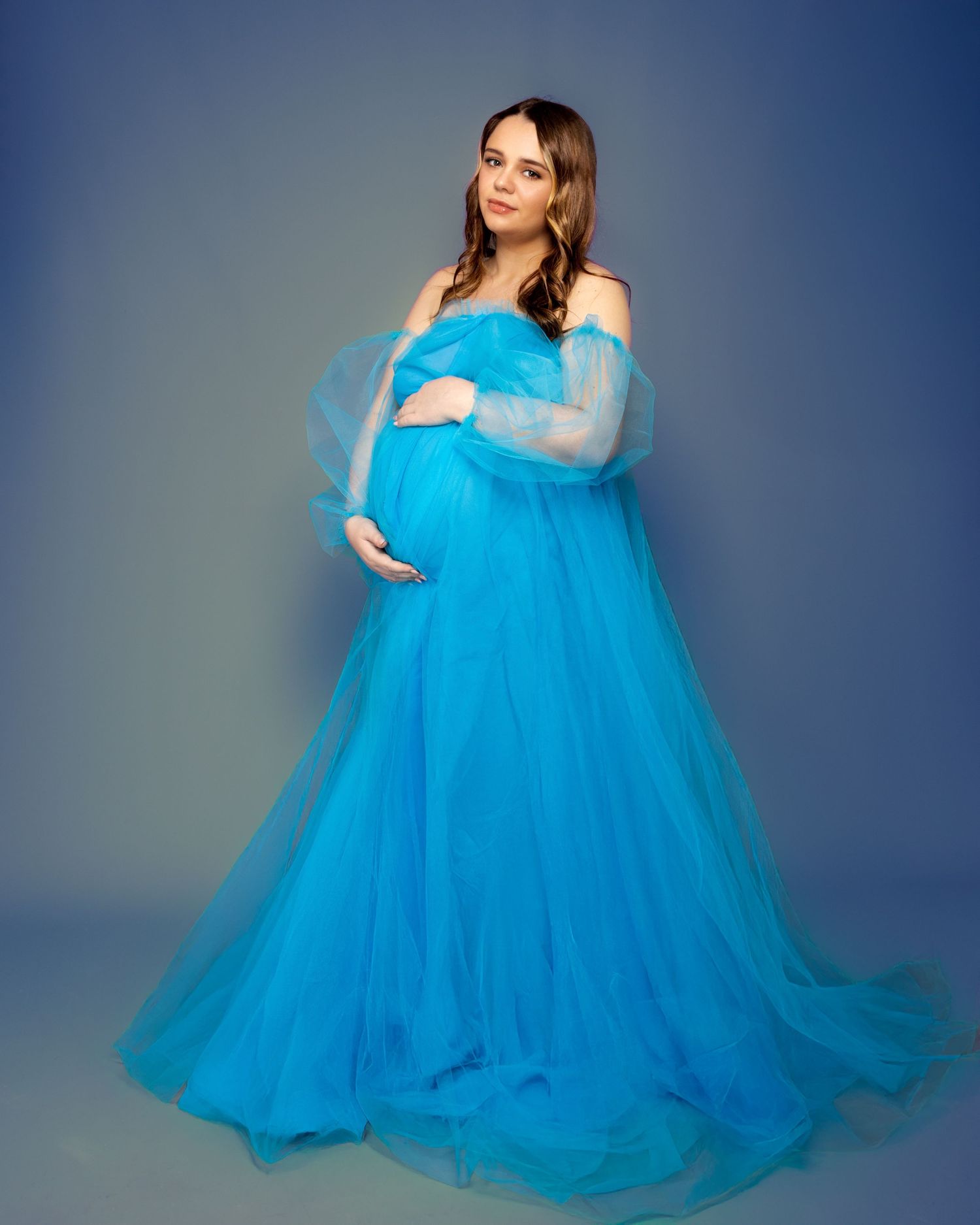 Maternity portrait in billowing turquoise tulle gown against blue studio background. female pregnancy photographer.