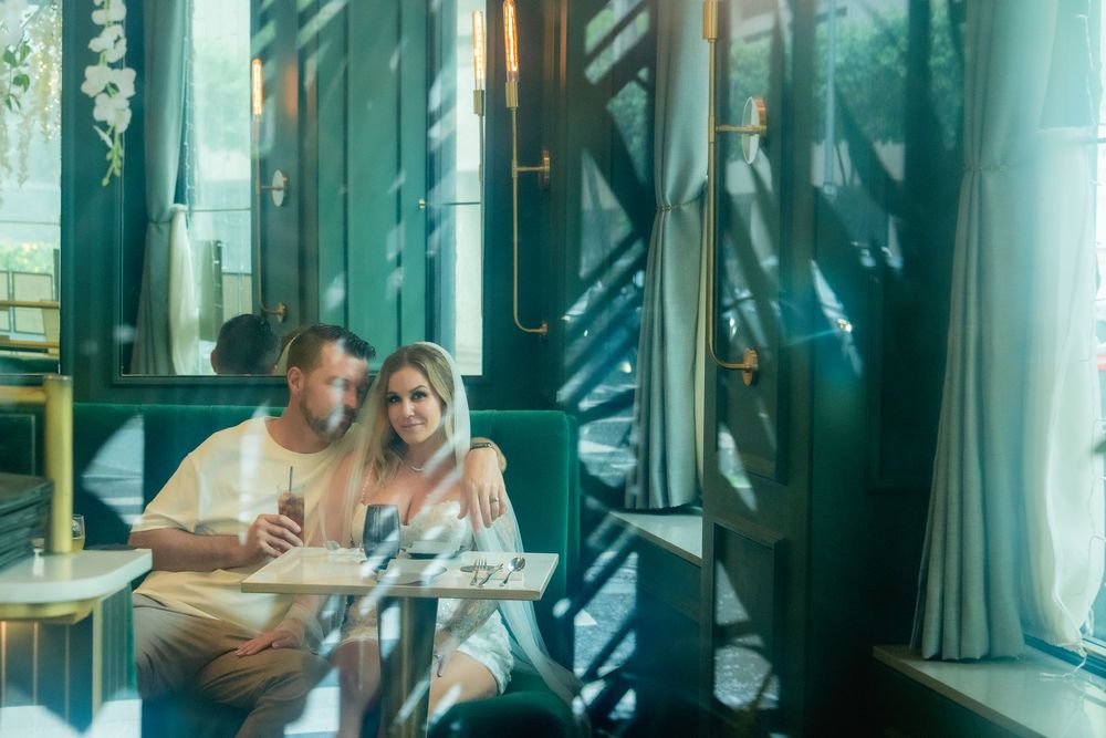 Newlyweds sitting in Podmore restaurant, photo taken outside the glass so there are reflections and sunlight and shadows on them.