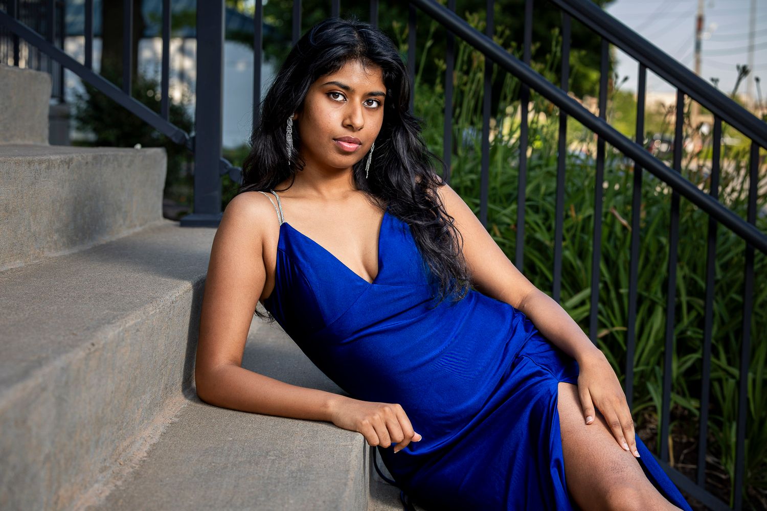 Young woman in elegant royal blue satin dress sitting gracefully on outdoor stone steps.