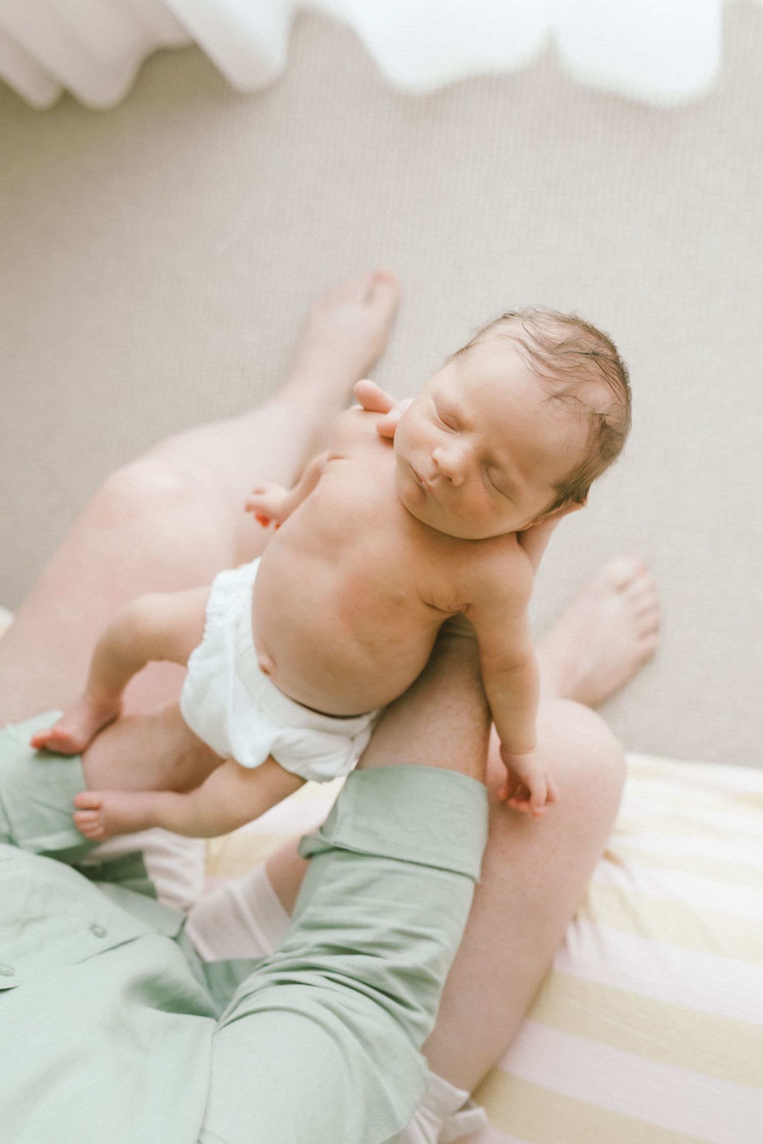 Newborn baby in diaper resting peacefully on parent's lap, soft natural light, tender family moment.