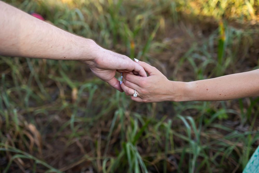 Couple holding hands outdoors in a green field, woman wearing an engagement ring, romantic connection.