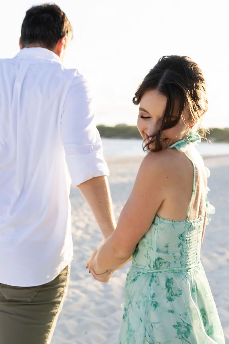 Couple holding hands walking on sandy beach during their engagement session.