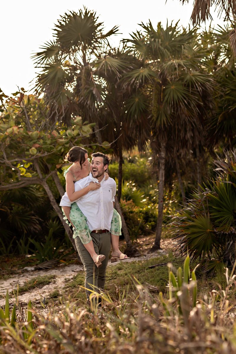 Man lifting woman in teal dress outdoors near tropical palm trees at golden hour.