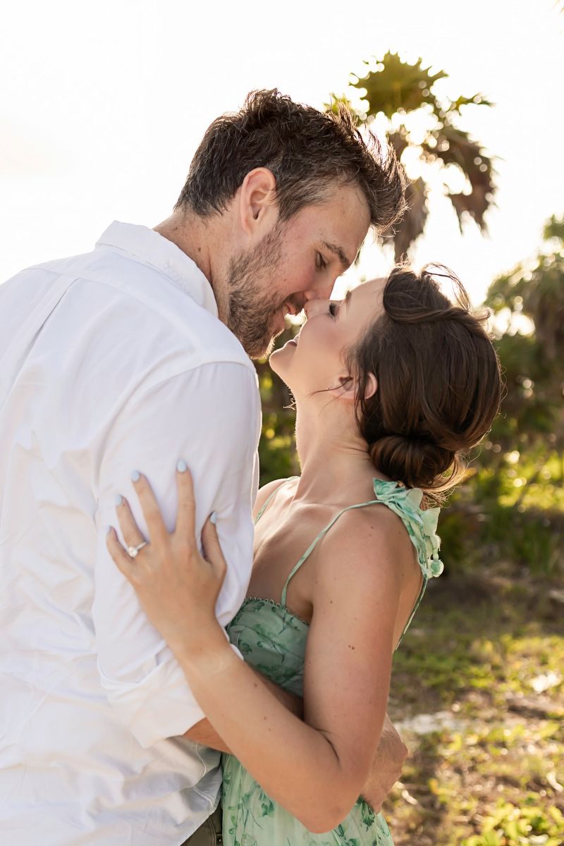 Couple sharing a romantic kiss outdoors with palm trees and golden sunlight in the background.