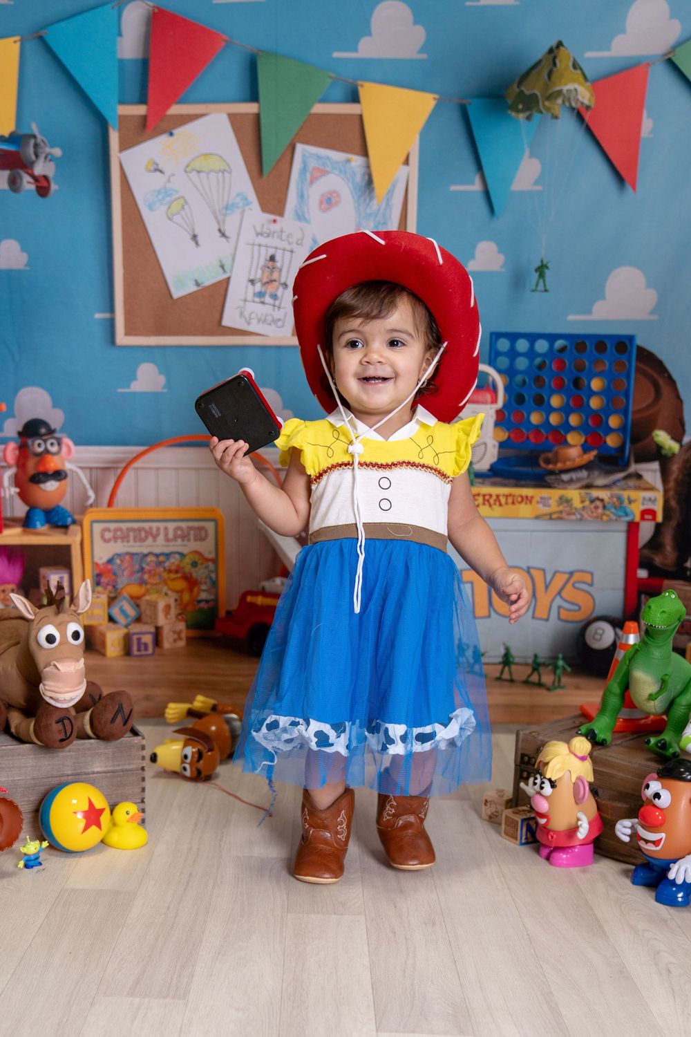 Toddler girl dressed as Jessie from Toy Story in colorful playroom with toys and bunting.