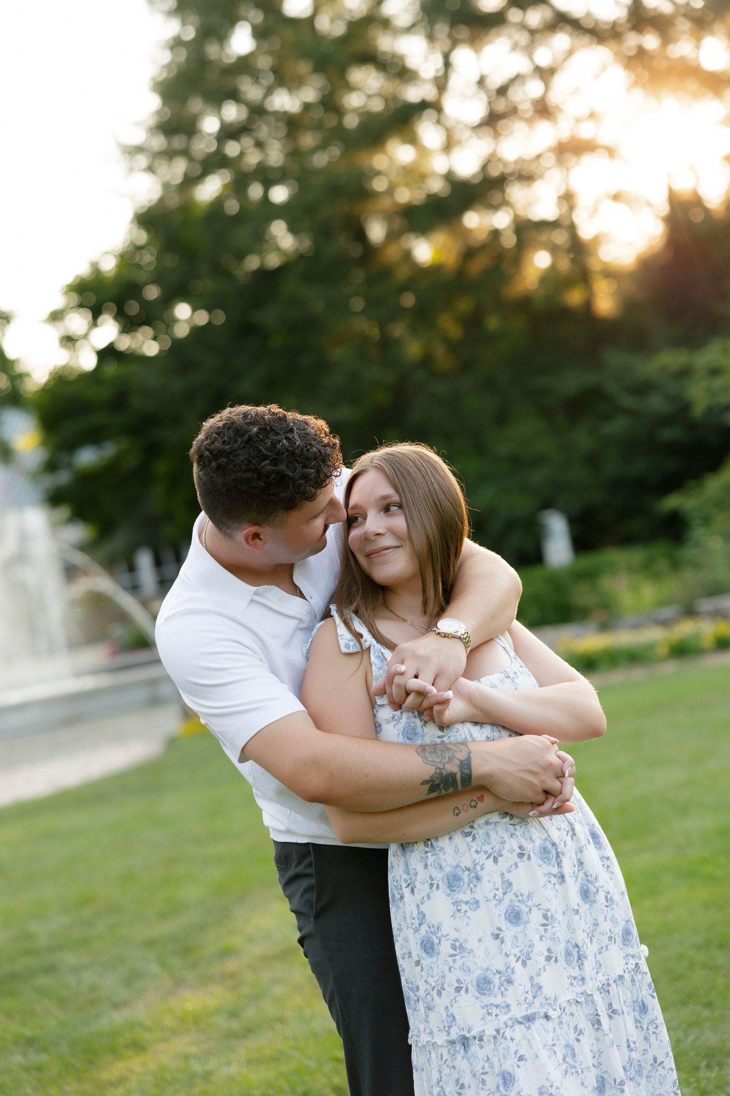 Couple embracing at golden hour in a lush garden park with a fountain in the background.