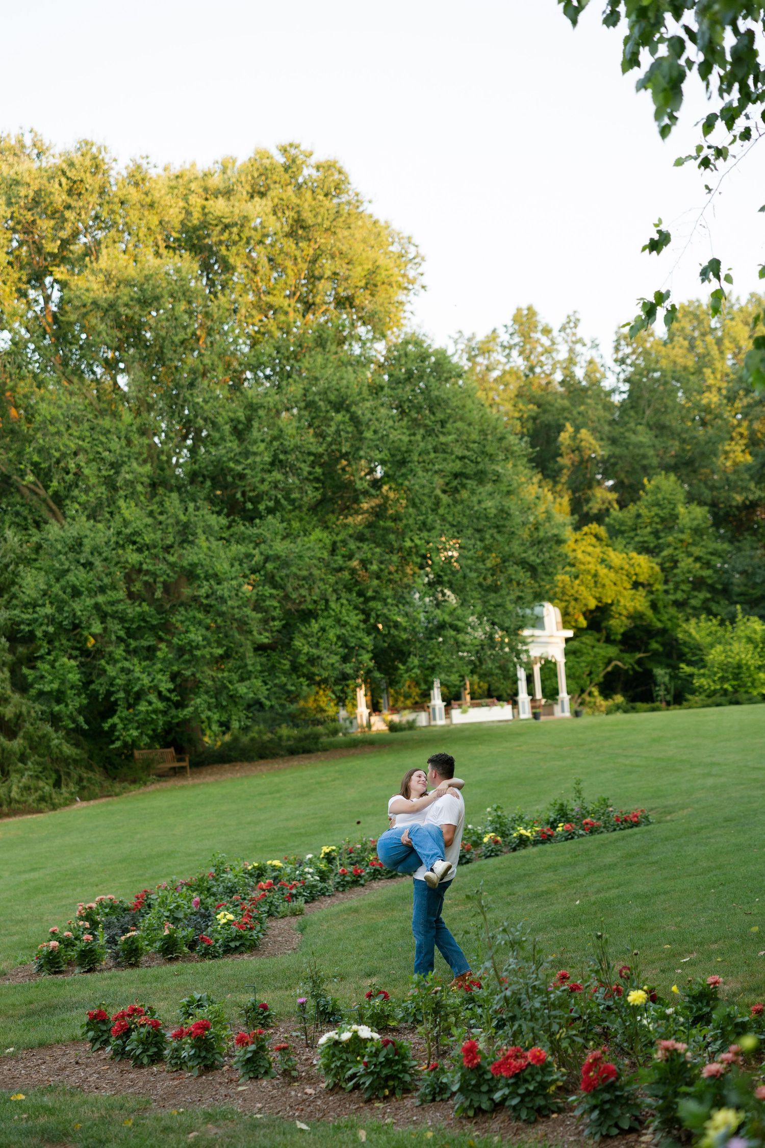 Man lifting woman in his arms among colorful flower beds in a lush green park.