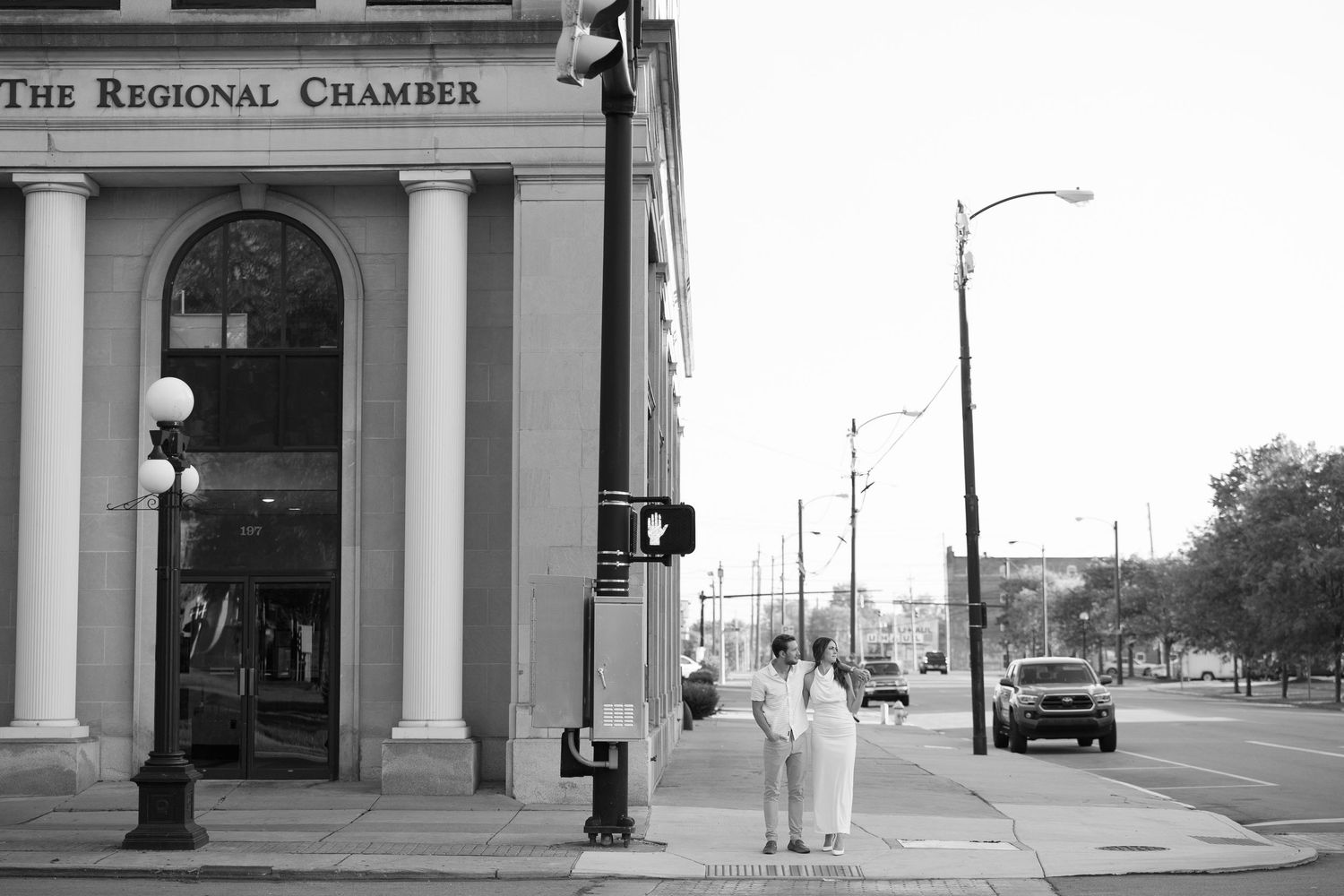 Black and white engagement photo of couple standing at a street corner near The Regional Chamber building.