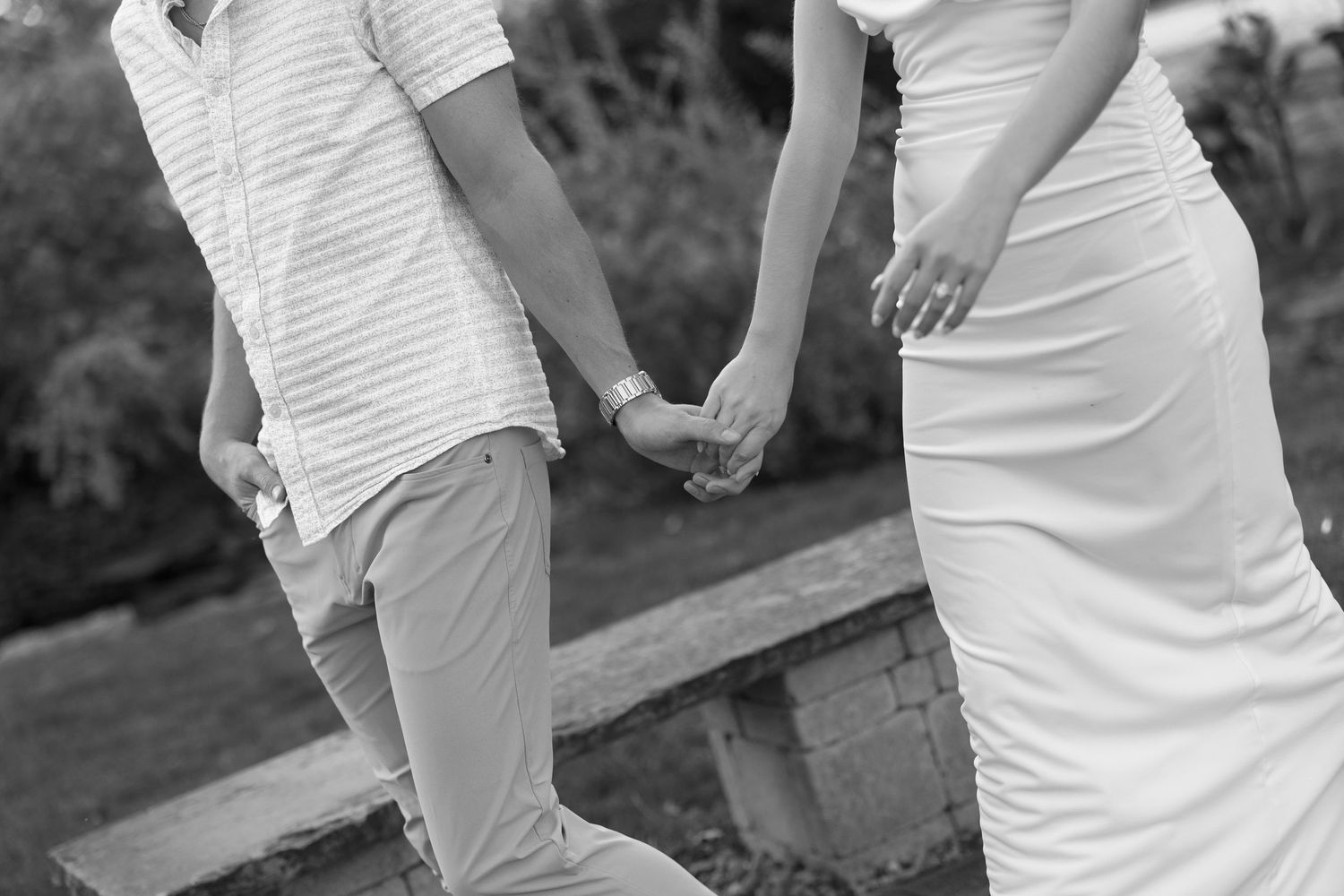 Black and white photo of a couple holding hands while walking through a park.