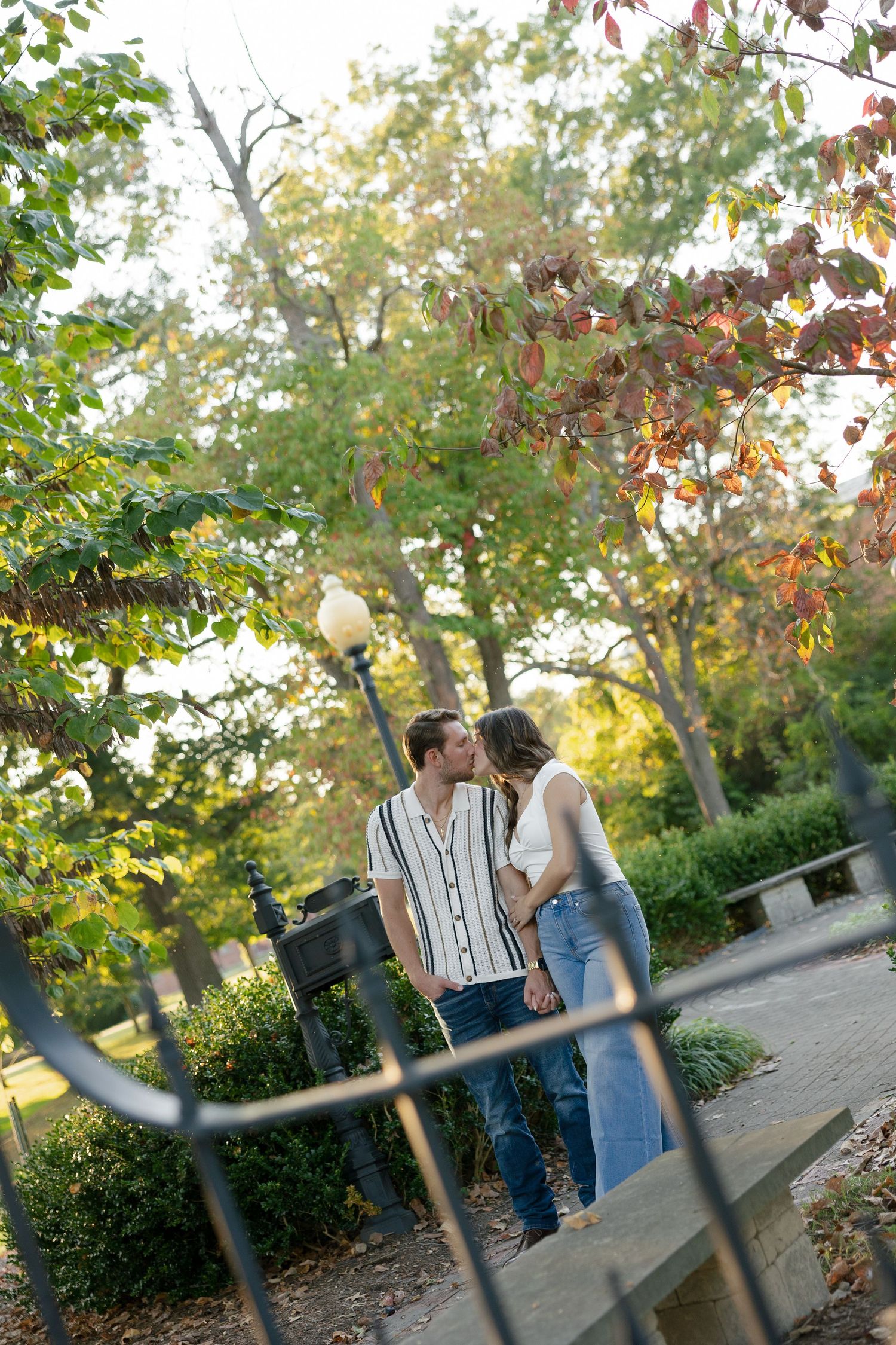 Couple sharing a tender kiss on a garden path framed by colorful autumn foliage.
