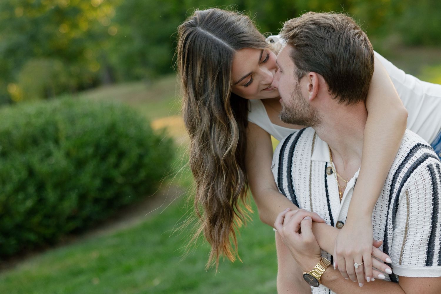 Man tenderly kissing woman on the forehead while embracing in a lush green park.