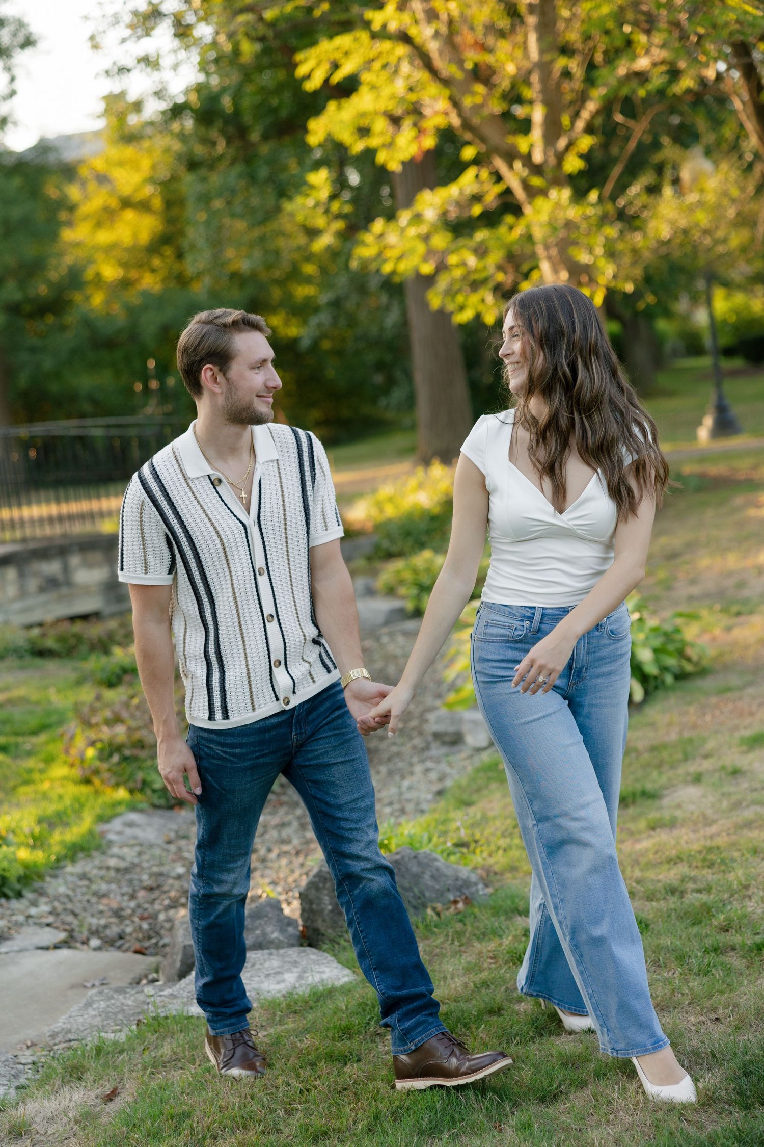Joyful couple holding hands and smiling at each other while walking in a sunny park.