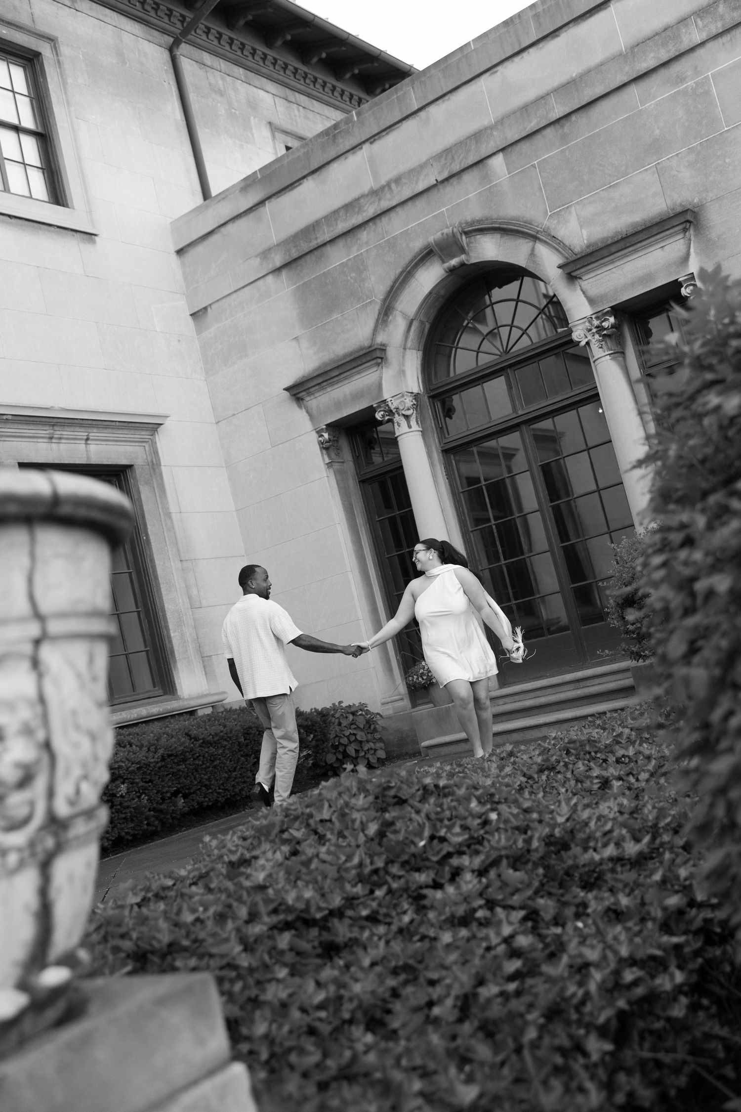 Black and white photo of couple holding hands walking toward a grand stone building exterior.