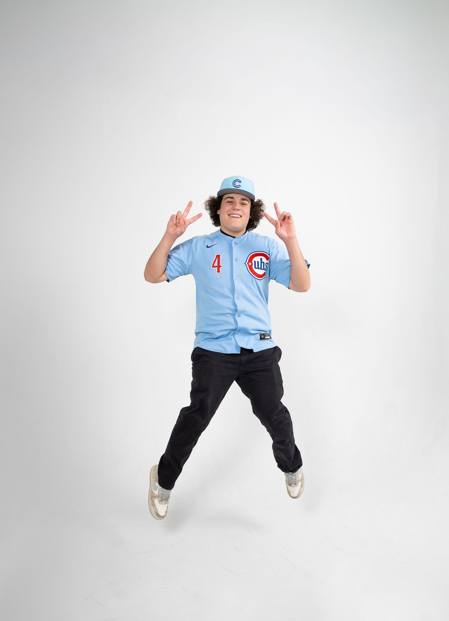 Energetic young man jumping in a Chicago Cubs light blue baseball jersey number 4 on white background.