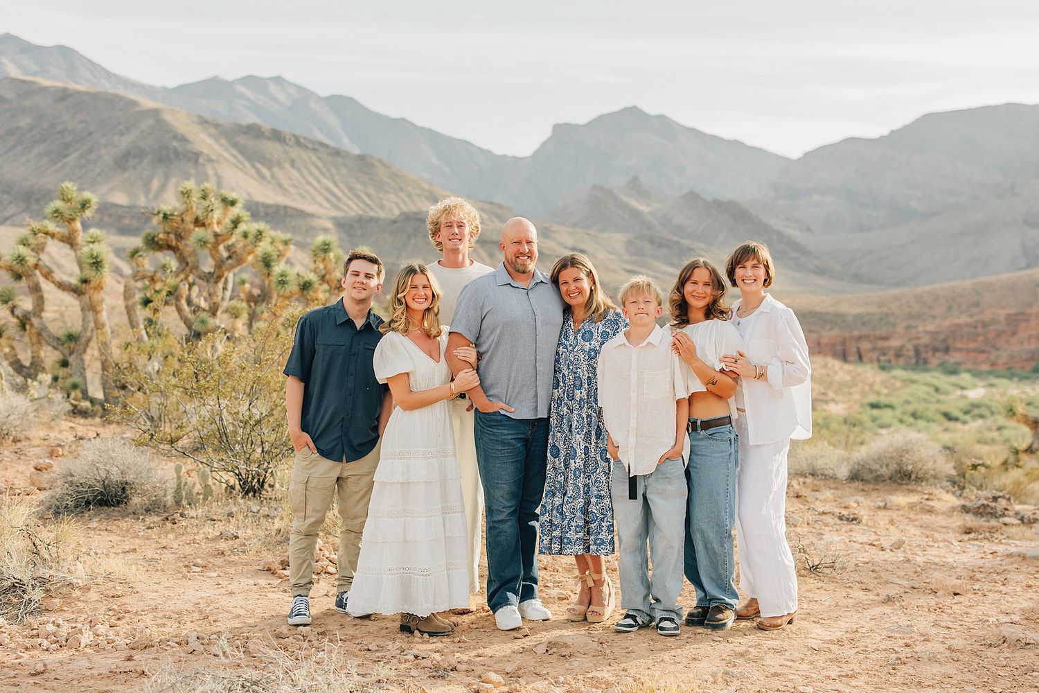 Family of eight posing together in desert landscape with mountains and Joshua trees in background.