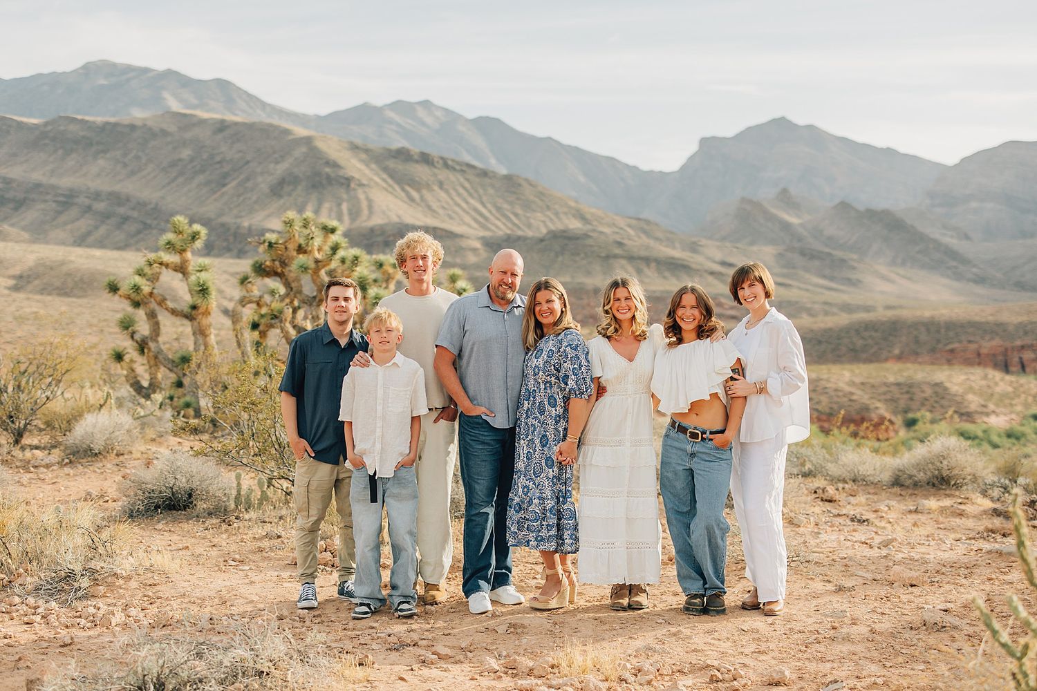 Family of seven posing together in desert landscape with Joshua trees and mountain backdrop.