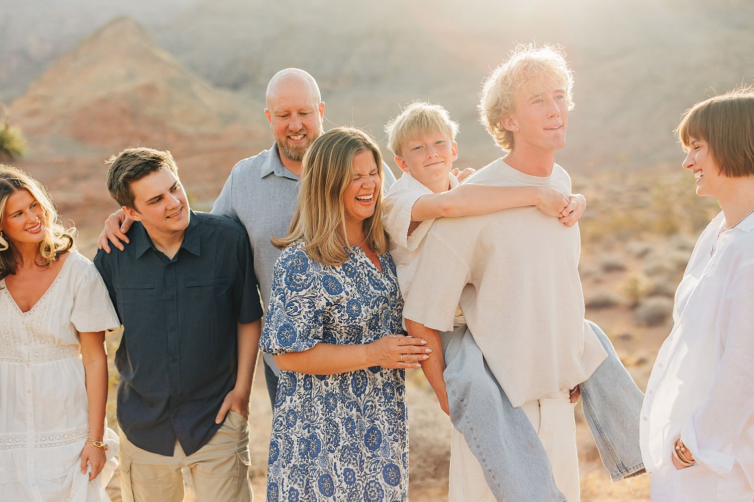 Family laughing together outdoors in golden desert light, casually dressed in neutral and blue tones.