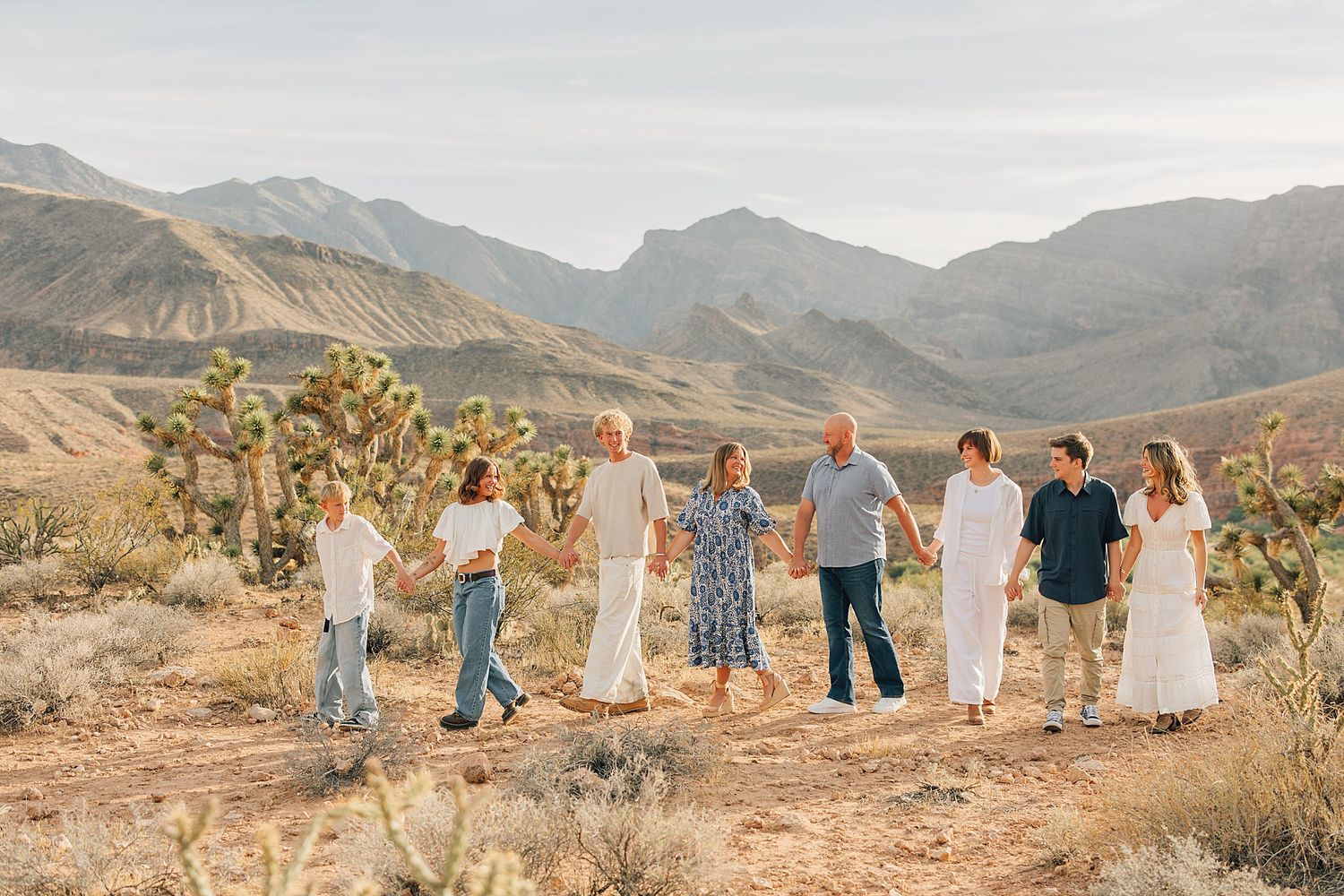 Extended family holding hands walking through desert landscape with Red Rock Canyon mountains behind.