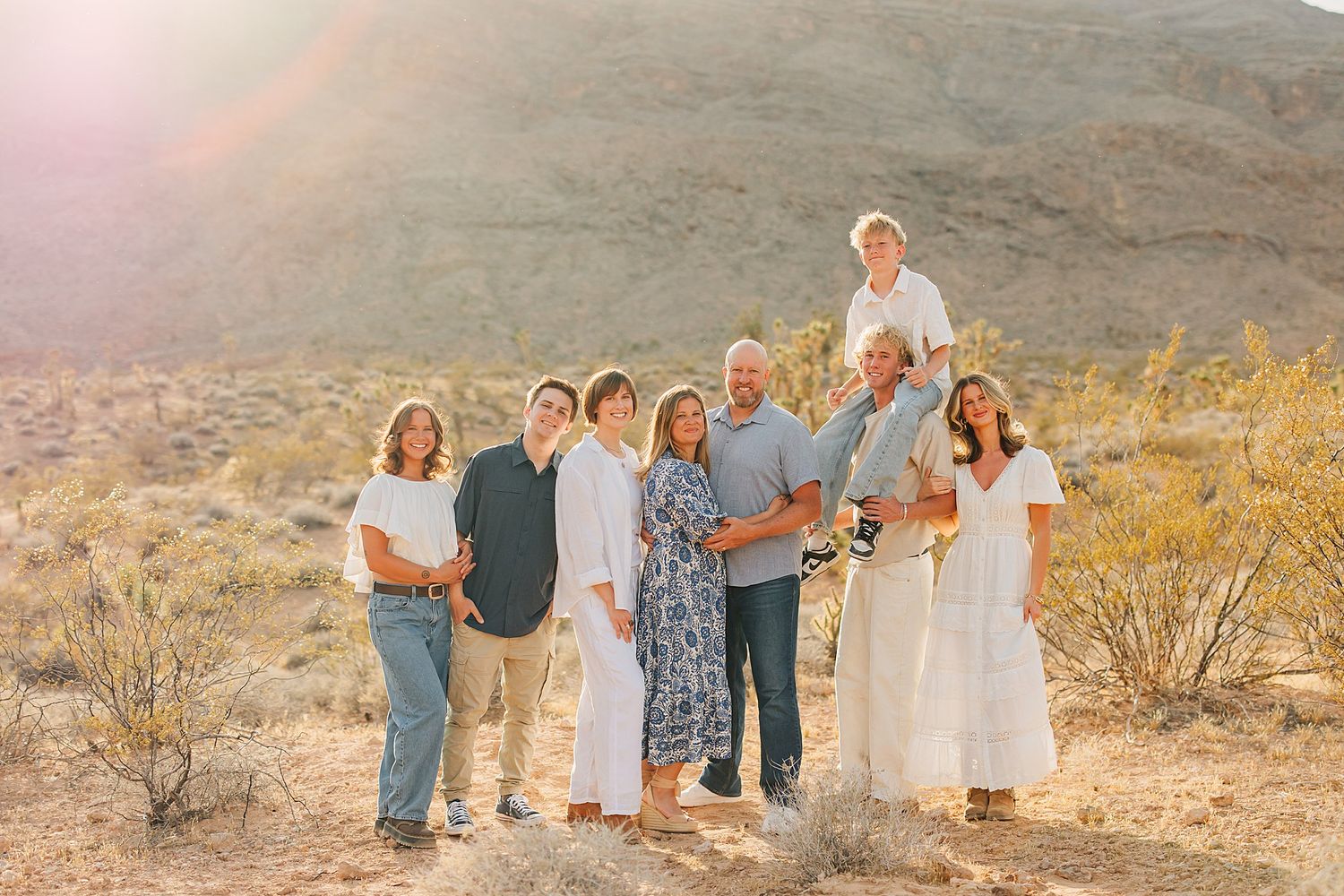 Family of eight posing together in a sunny desert landscape with mountains in the background.