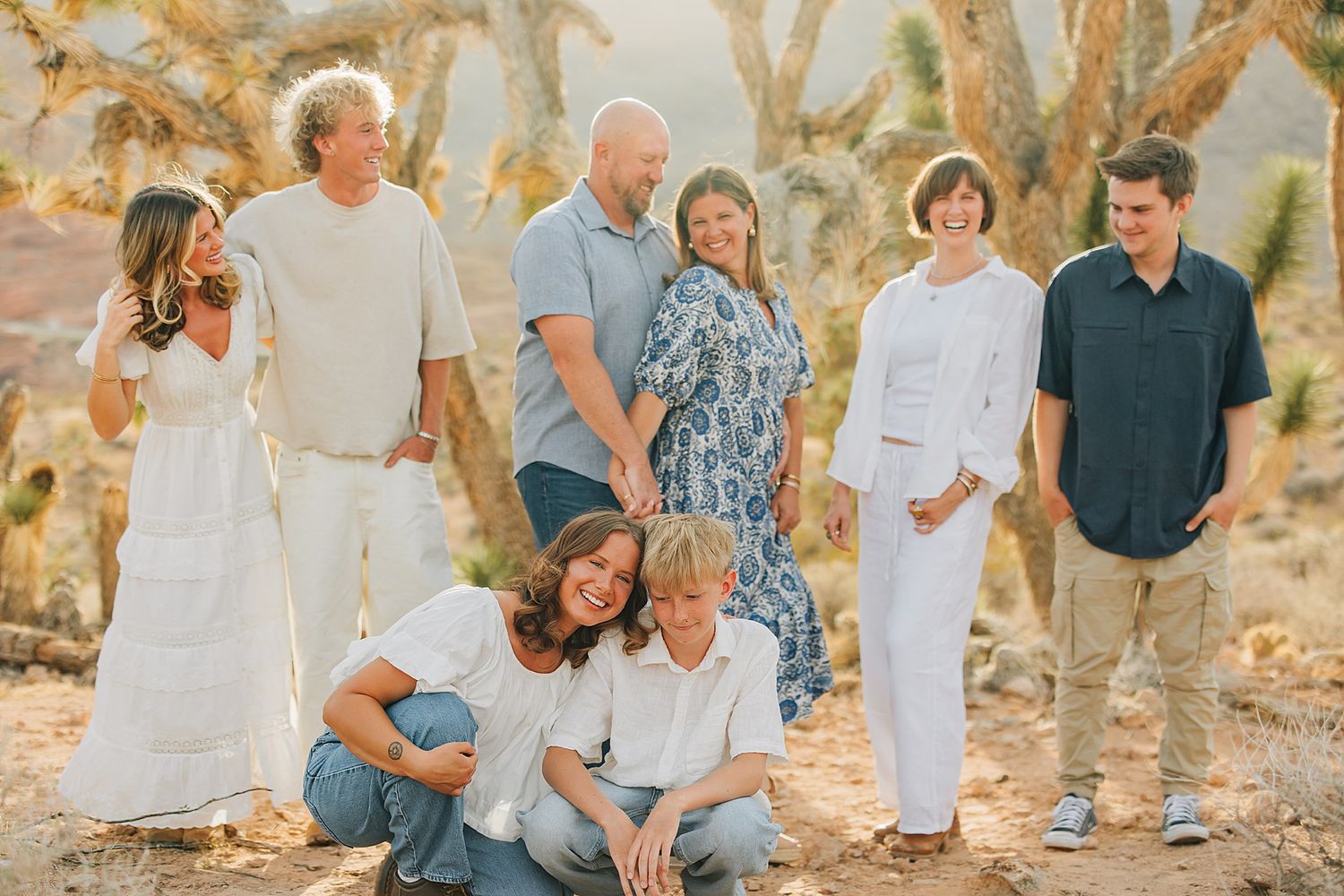 Family group portrait of eight people posing outdoors in desert landscape with Joshua trees in warm golden light.