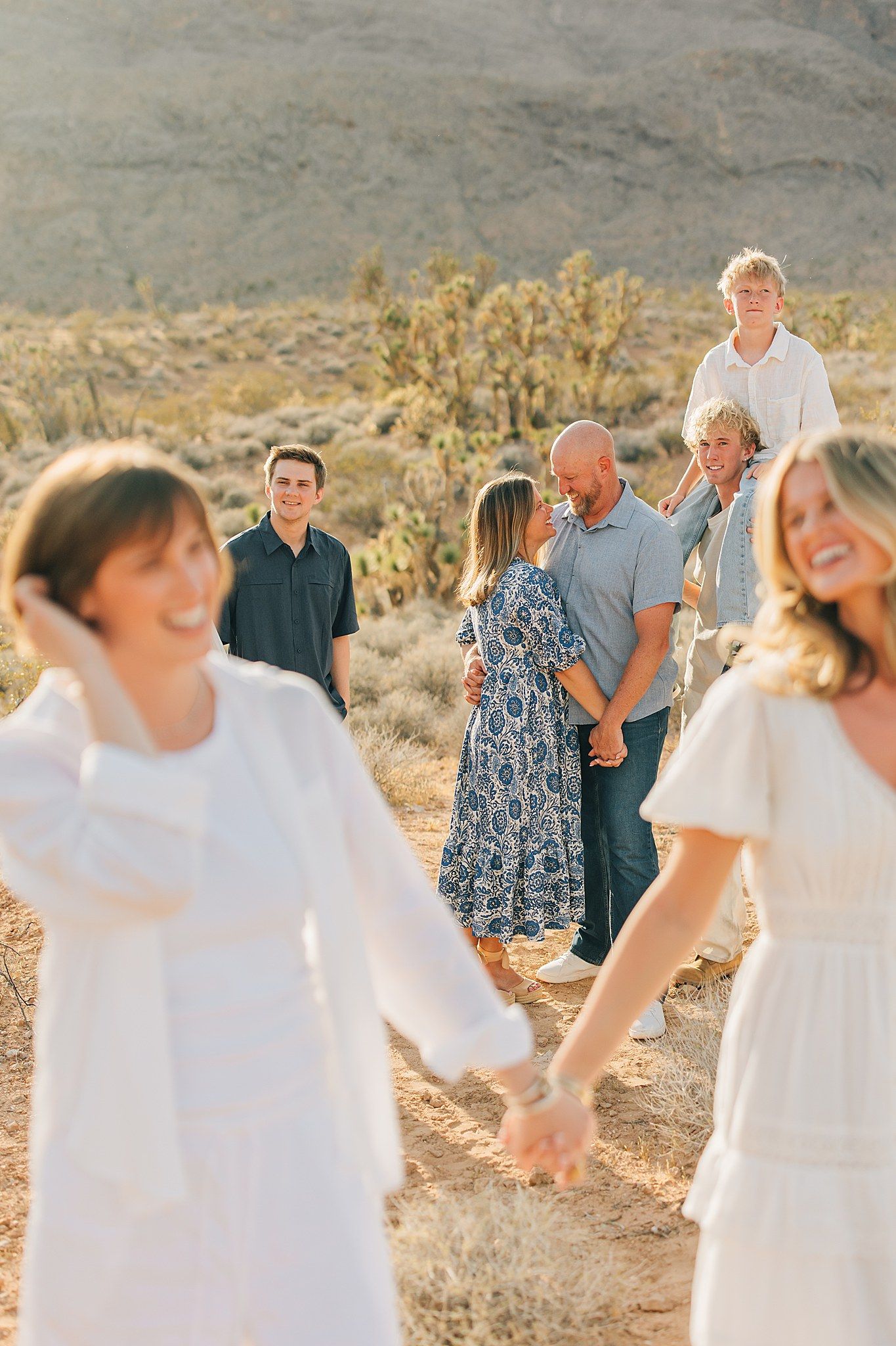Family gathering in desert landscape, couples holding hands with children smiling in golden hour light.