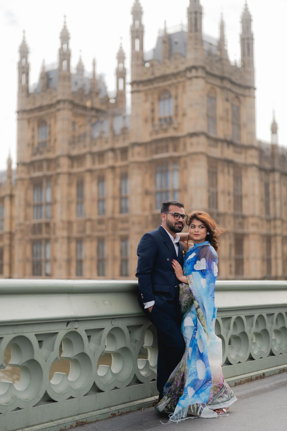 Couple posing on Westminster Bridge with the Houses of Parliament in London backdrop, woman in blue saree.