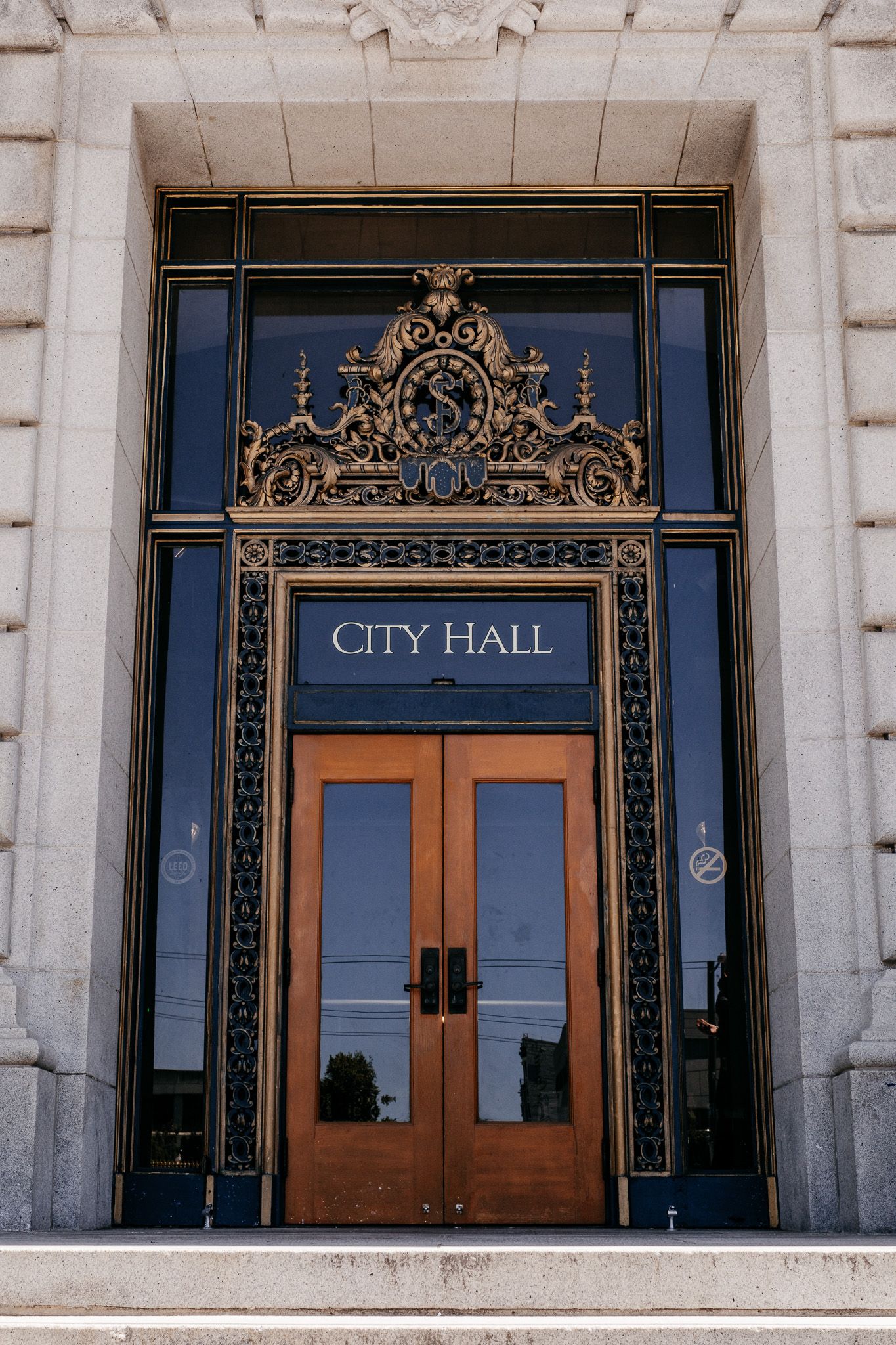Ornate City Hall entrance with decorative gold metalwork, wooden doors, and classical stone architecture.