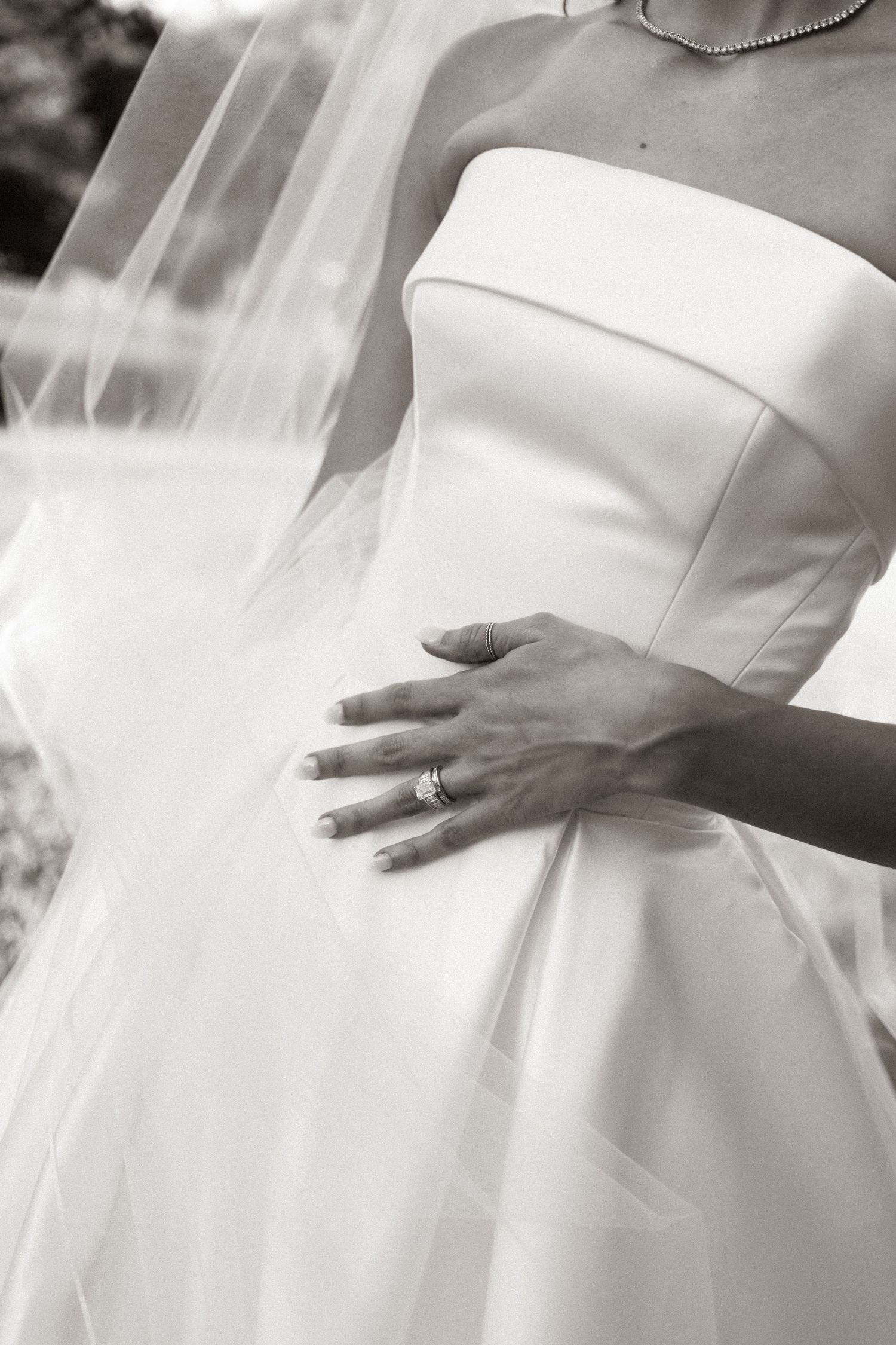 Black and white photo of a bride in a strapless wedding gown with veil, showcasing her diamond ring.