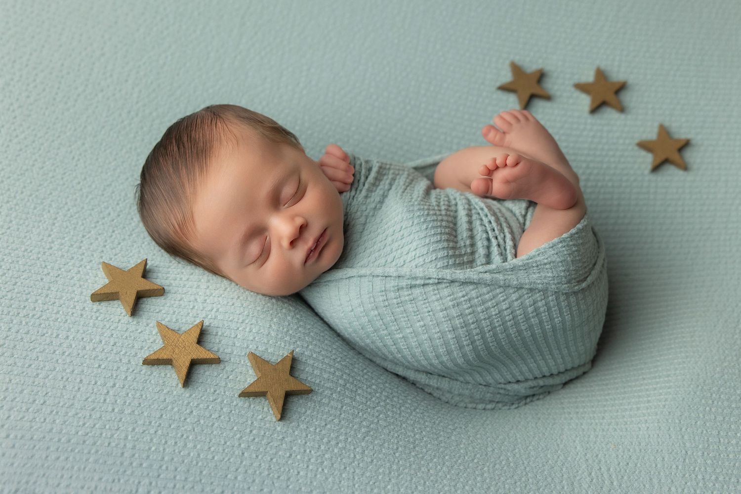 Peaceful newborn baby swaddled in cream wrap sleeping on soft beige blanket during professional newborn photography session.