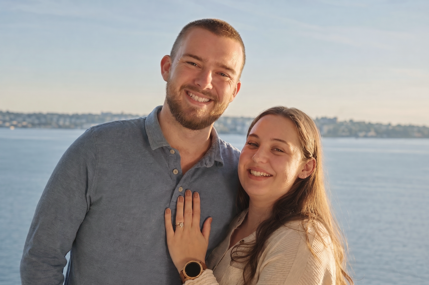 A young couple poses outdoors by the water during an engagement photo shoot.