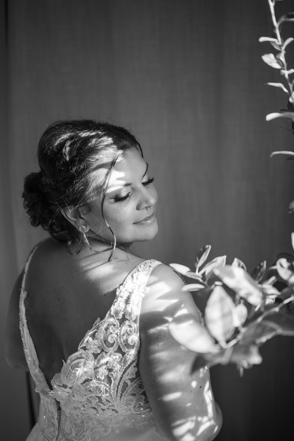 Black and white bridal portrait of a bride in lace gown holding bouquet, bathed in soft natural light.