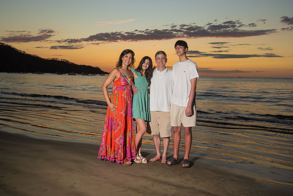 Couple smiling at each other surrounded by lush tropical greenery, woman in floral dress, man in white shirt.