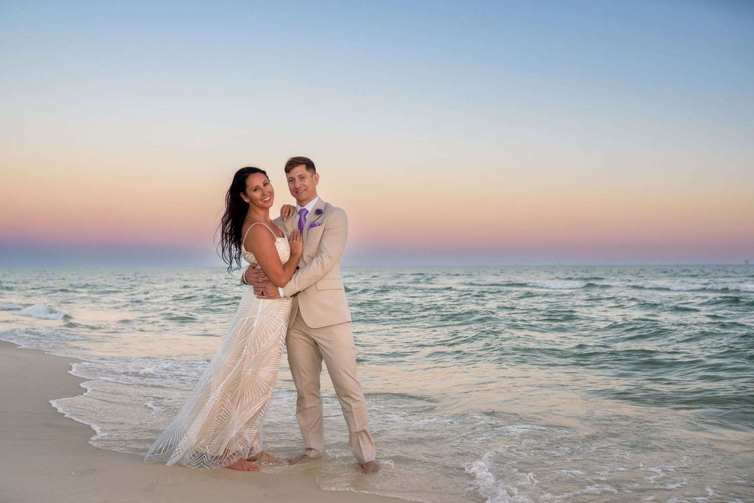 Romantic wedding couple embracing during a Dauphin Island beach sunset with soft golden light, ocean waves, and intimate Alabama Gulf Coast