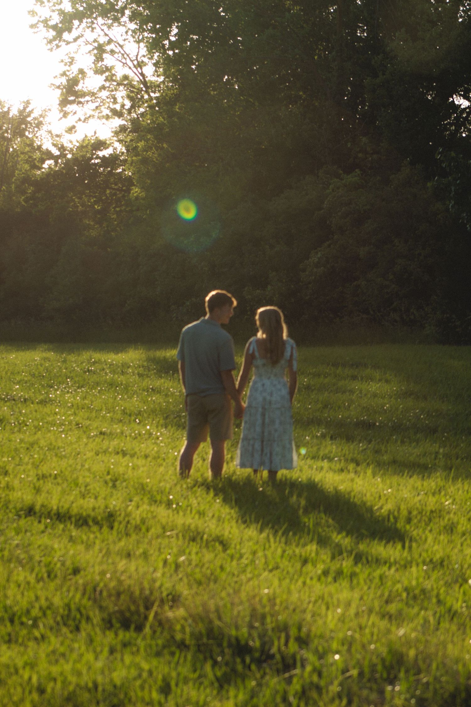 a couple sitting in a grassy field looking at the tree line