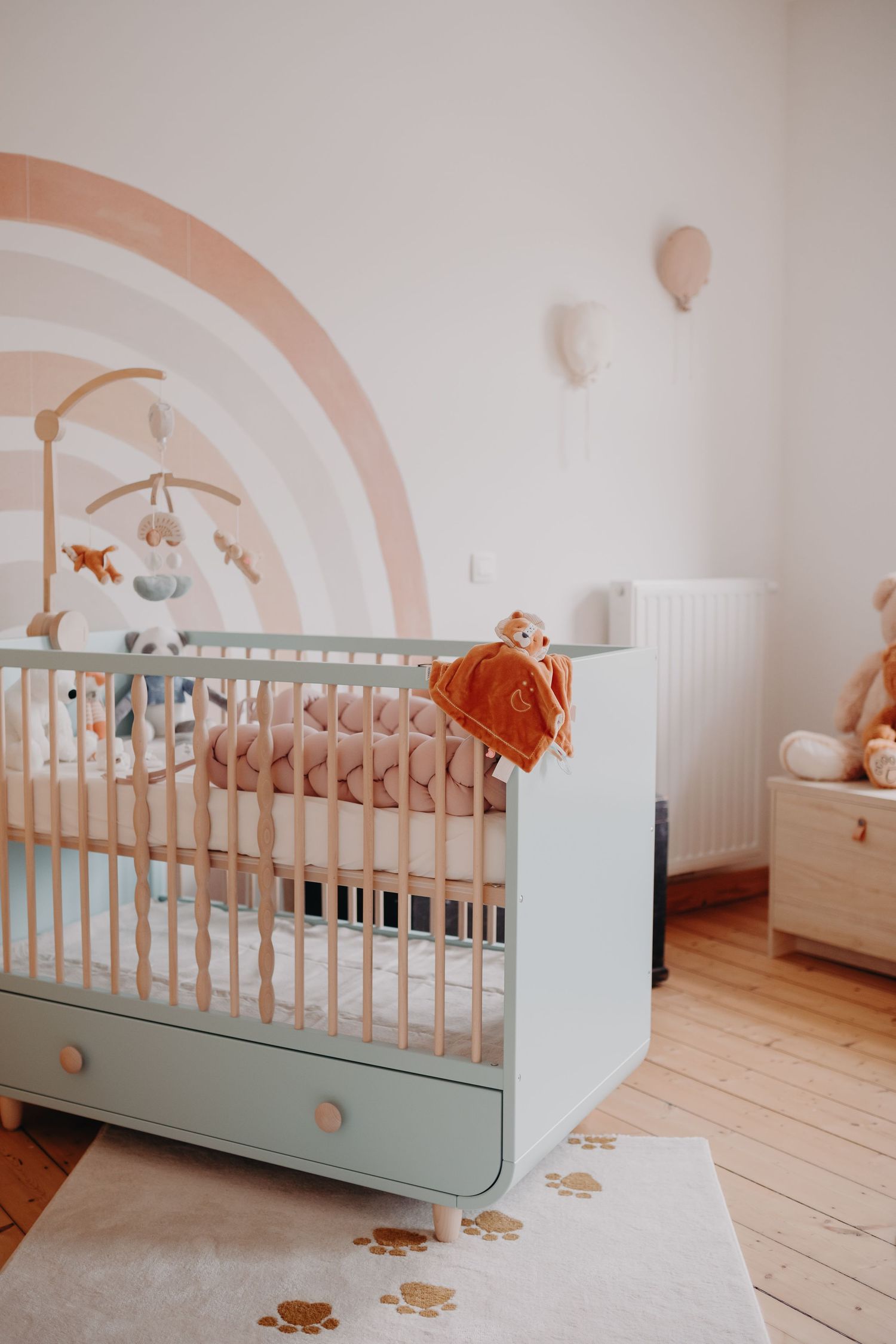 Pastel nursery with a mint green crib, rainbow wall mural, and baby toys.