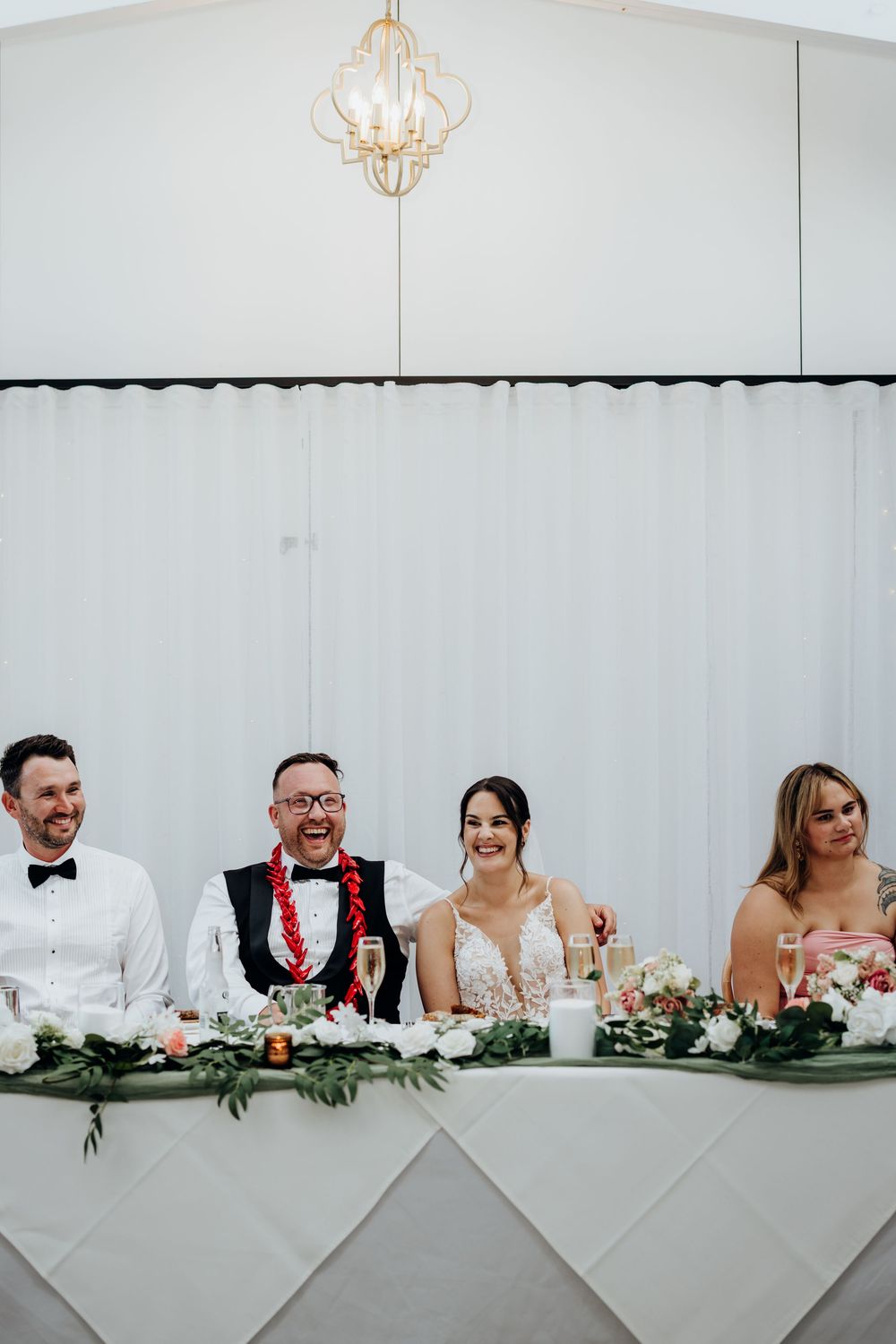 Bride and groom laughing joyfully at the head table during their wedding reception with floral arrangements.