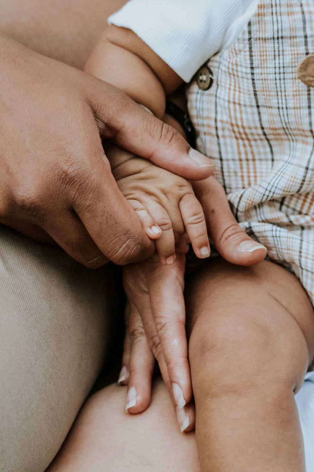 Close-up of an adult gently holding a baby's tiny hand, showing a tender bonding moment between parent and child.