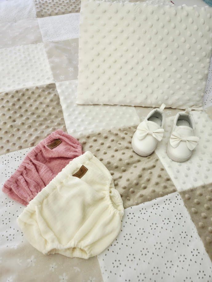 Soft baby girl set with cream bloomers, pink top, white bow shoes, and a patchwork minky blanket in neutral tones.