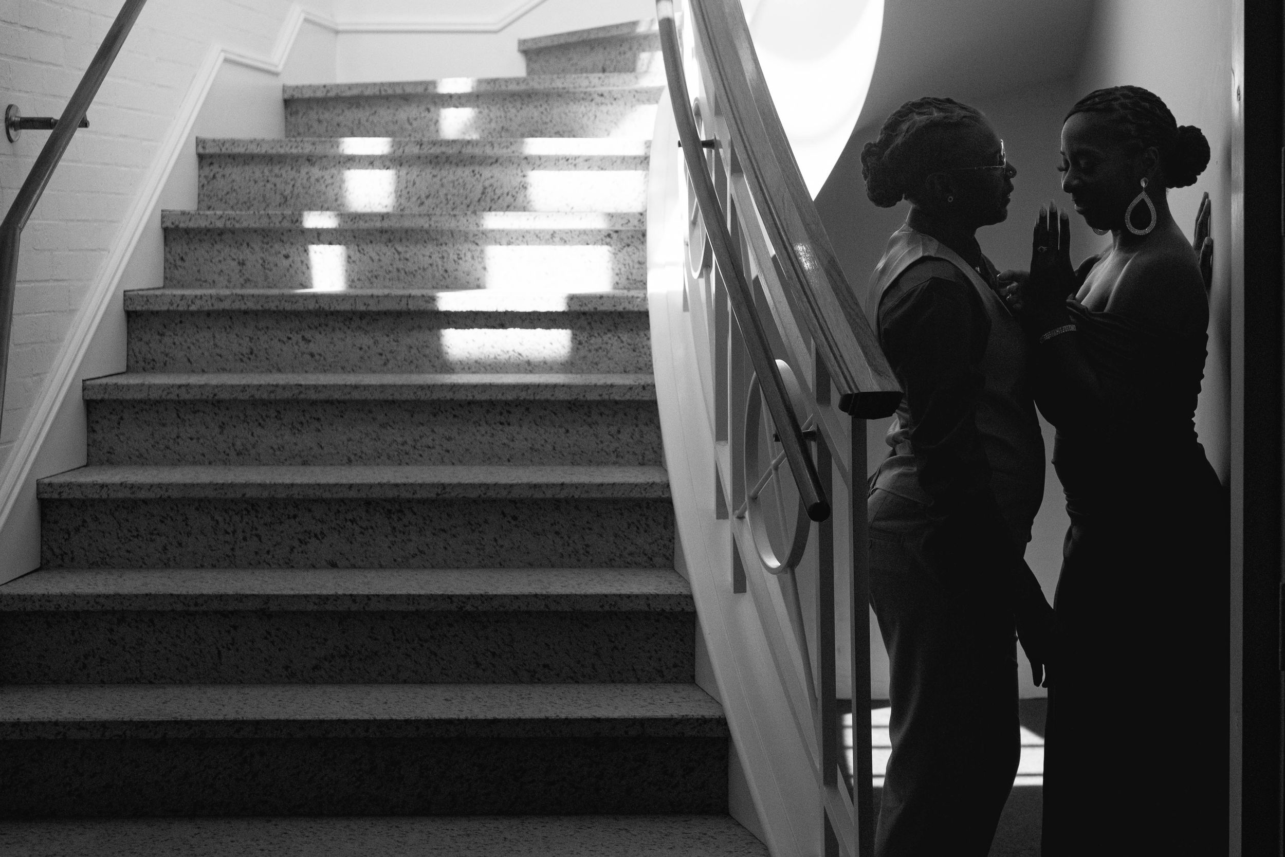 Silhouette of two women talking near a staircase in black and white photography.