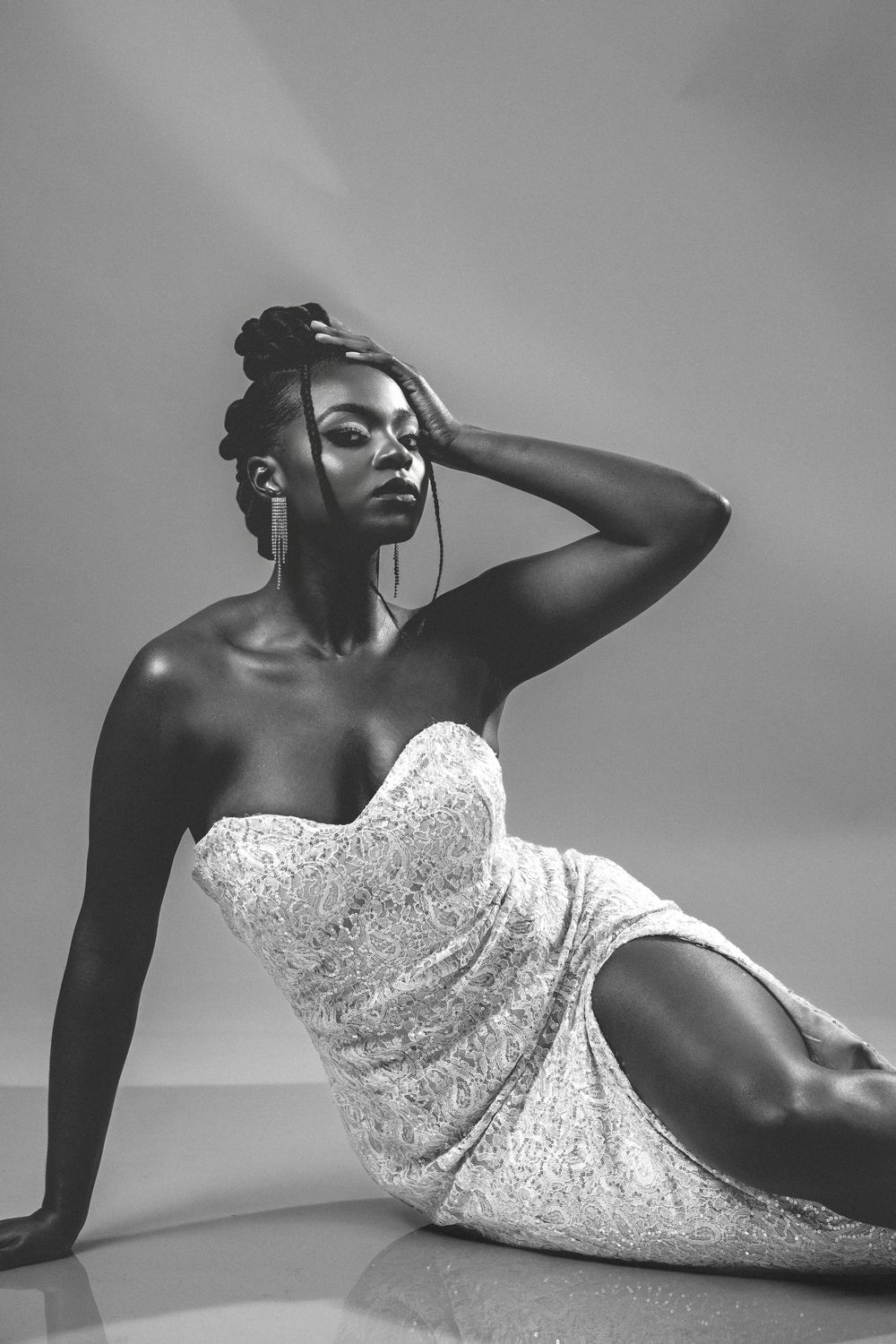 Black and white portrait of a woman in a strapless dress sitting gracefully on the floor with hand raised to her head.