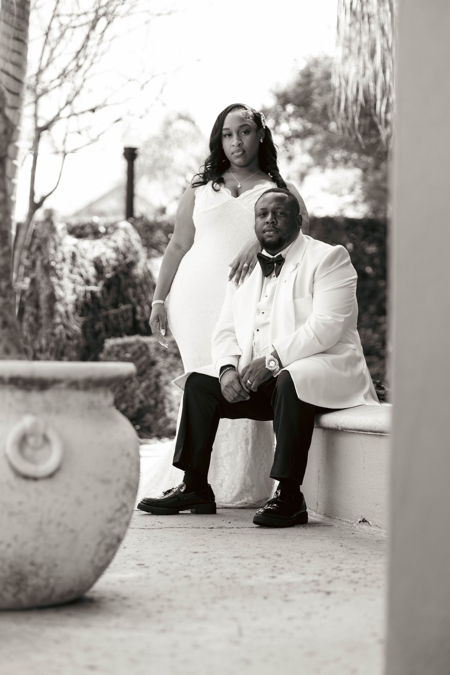 Black and white portrait of bride and groom posing in matching white outfits outdoors.