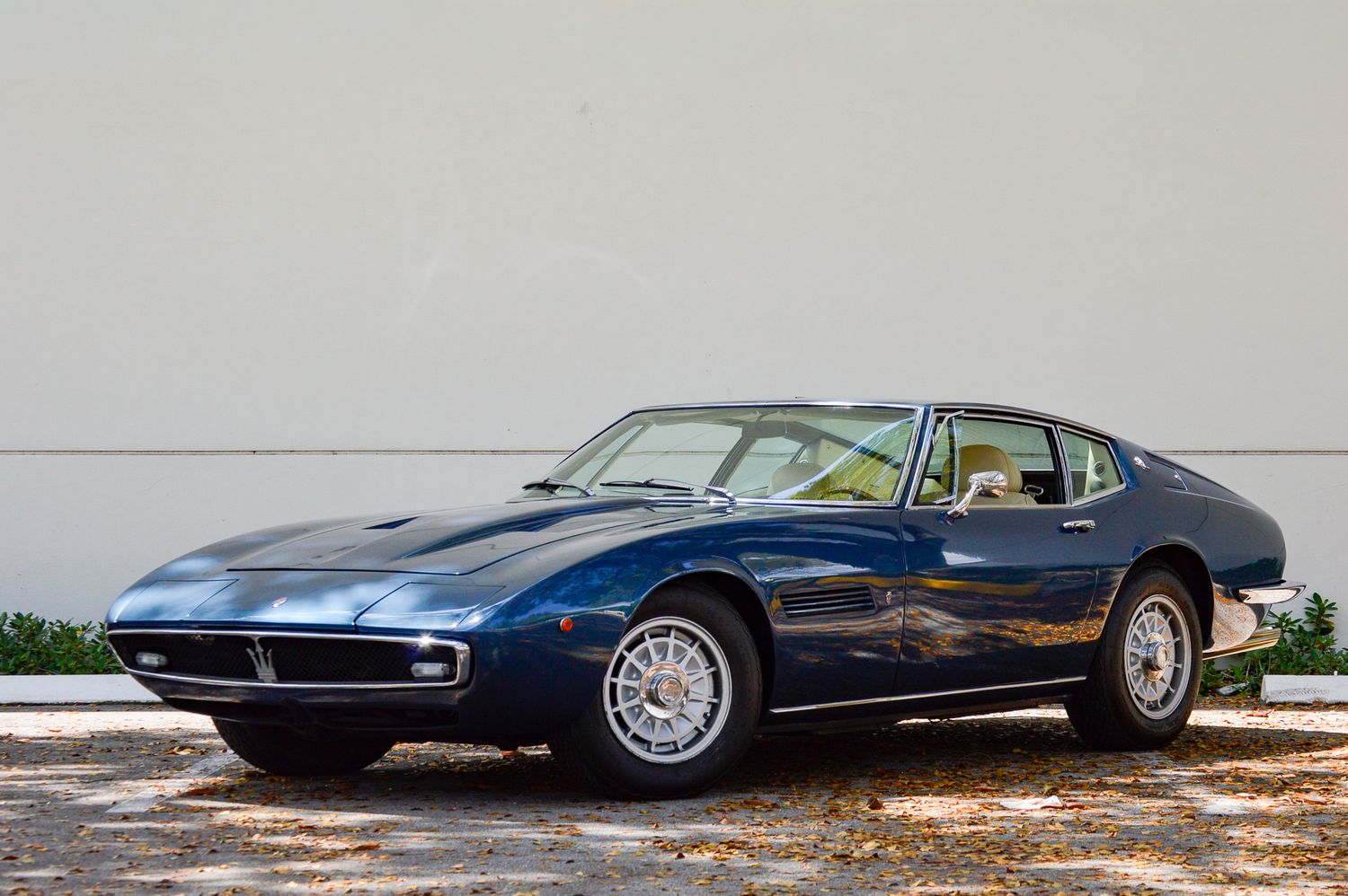 A classic navy blue Maserati Ghibli coupe parked outdoors, showcasing its sleek Italian design and chrome alloy wheels.