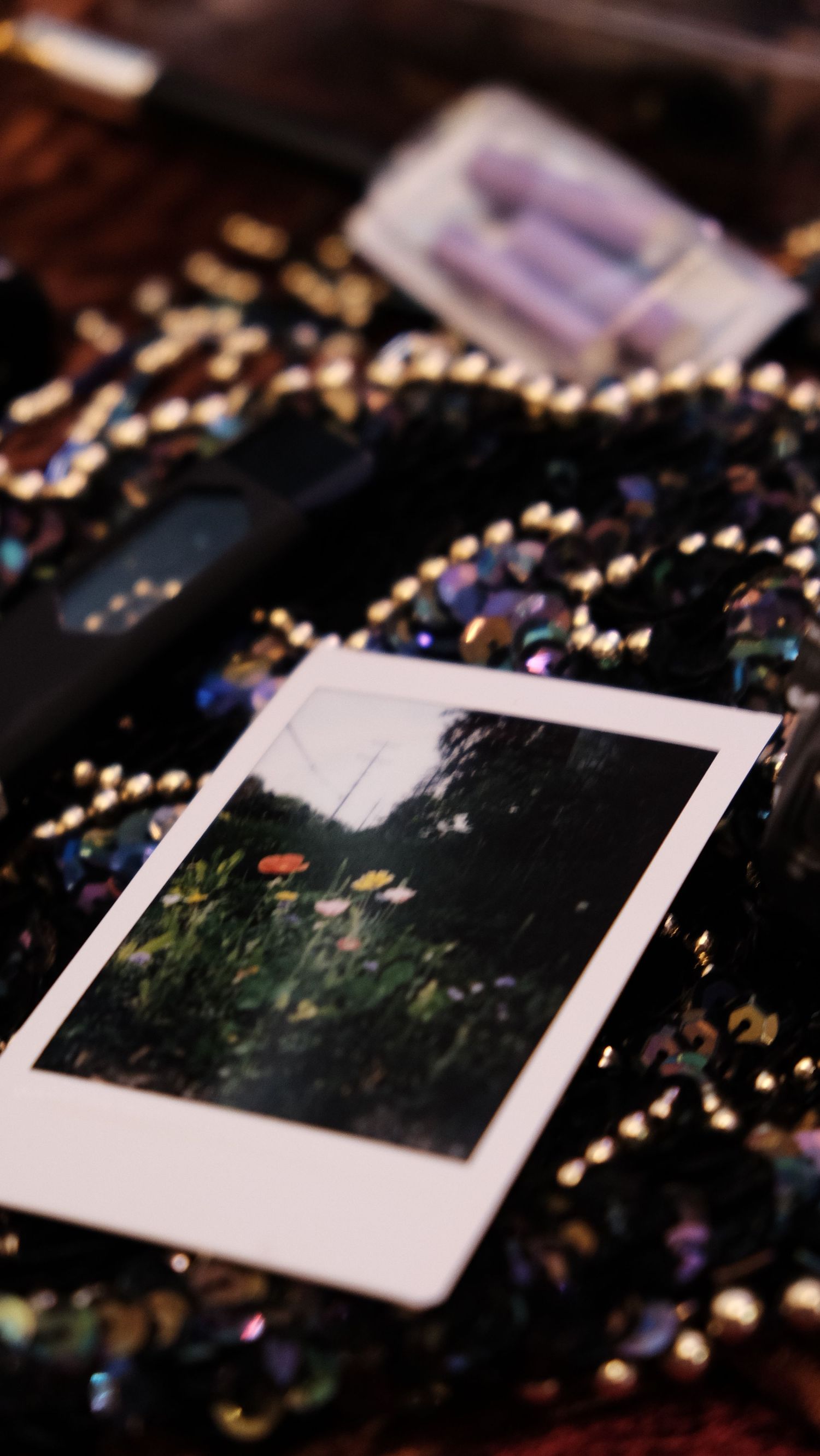Instax mini photo of wildflowers on a sequined surface with batteries and a black object in the background.