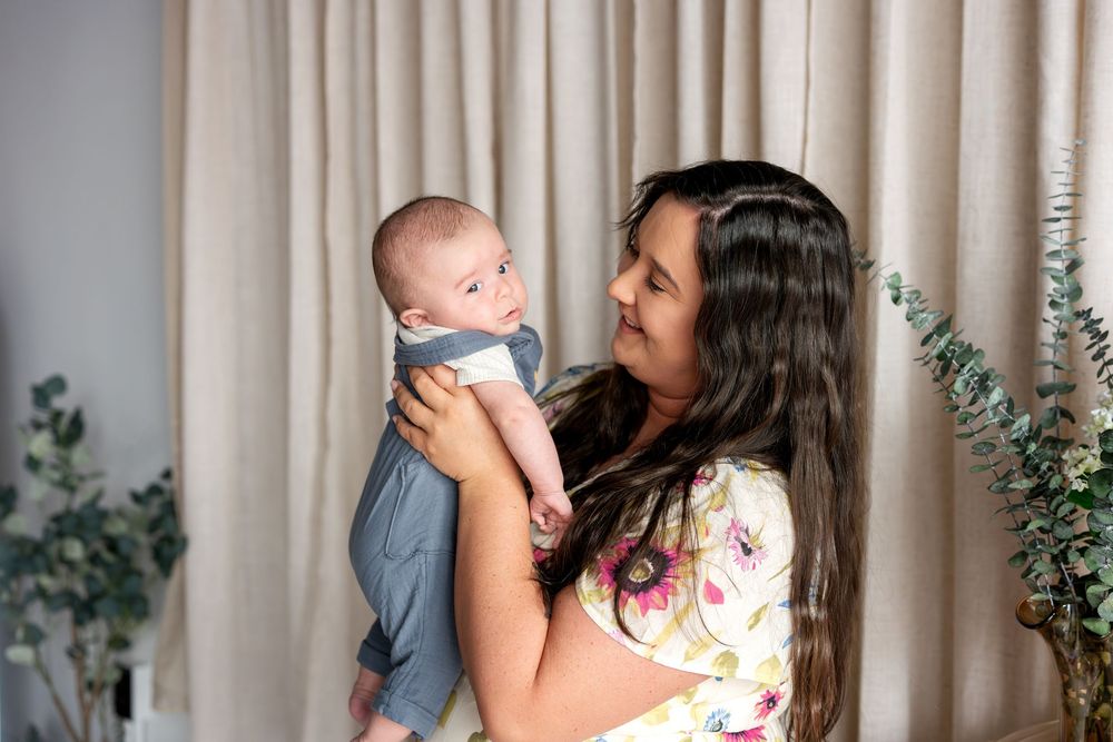 Brunette mother in floral dress holding and gazing lovingly at her alert newborn baby boy.