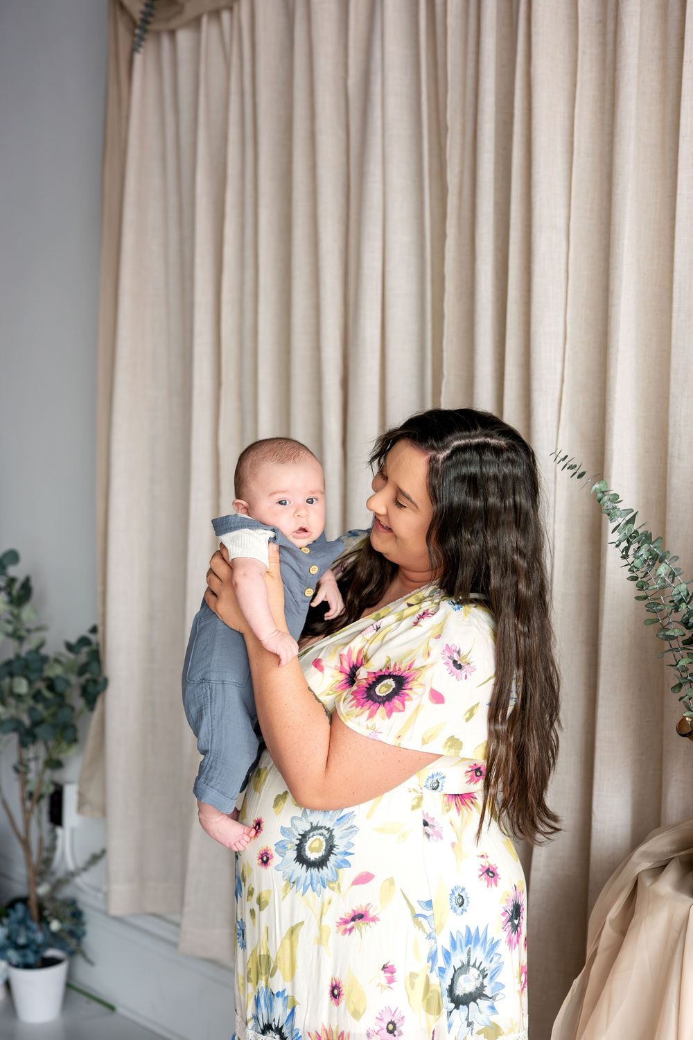 Smiling brunette mother in floral dress cradling and looking tenderly at her newborn baby boy.
