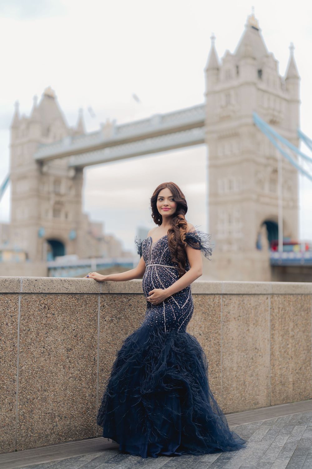 Pregnant woman in navy blue gown posing in front of Tower Bridge, London.