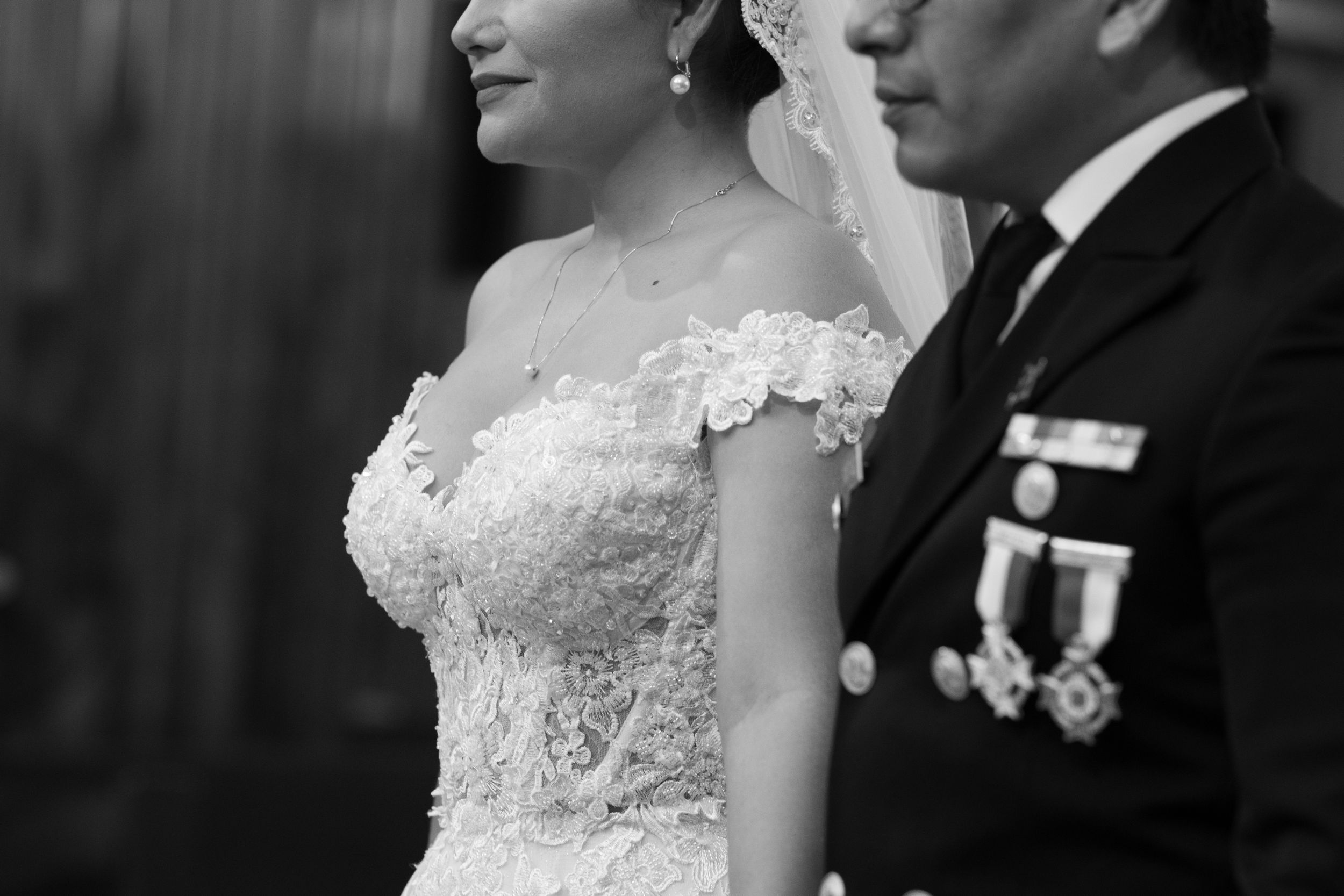 Black and white wedding photo of bride in lace off-shoulder gown beside groom in military uniform with medals.