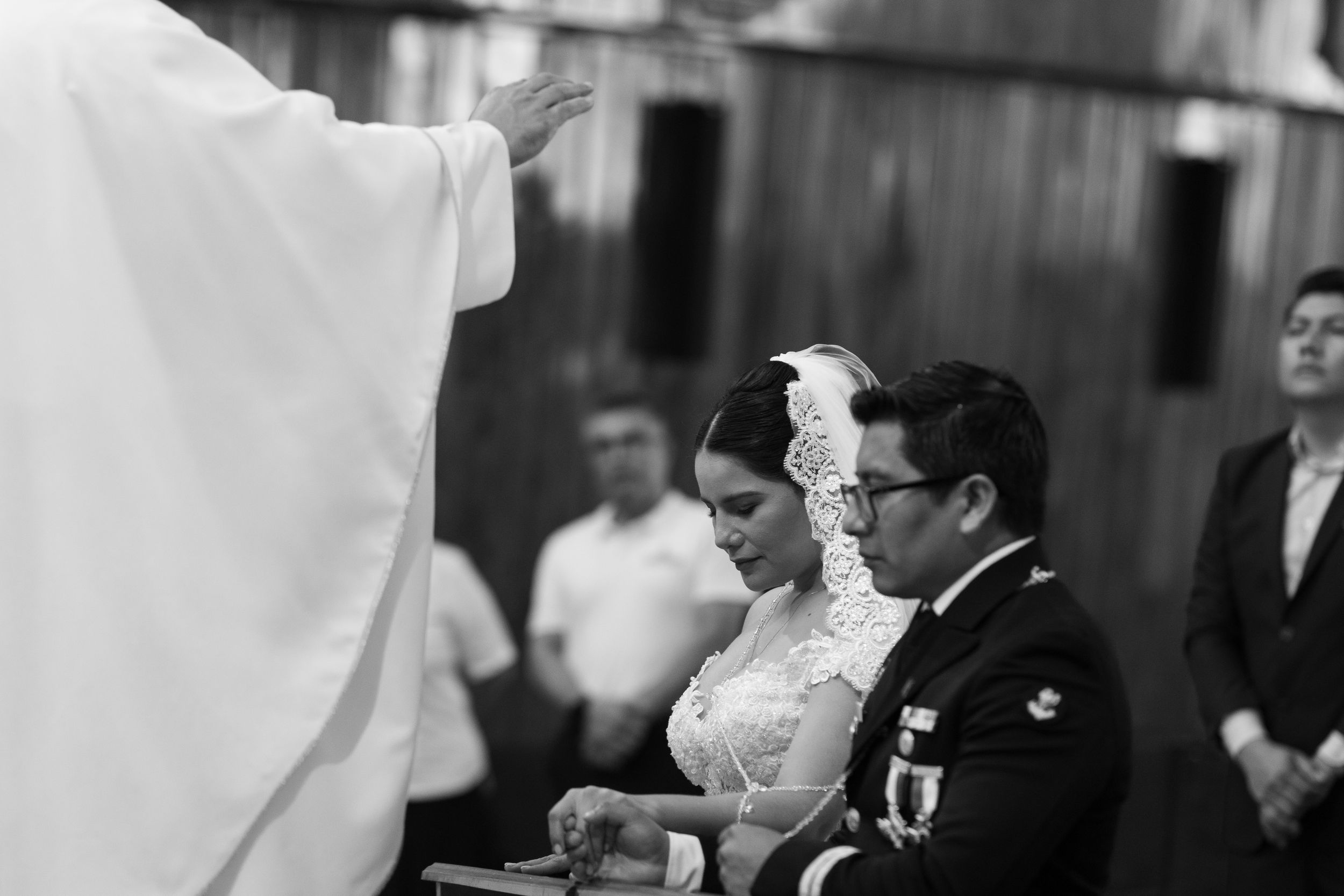 Black and white photo of a couple exchanging wedding vows before a priest at a church altar ceremony.