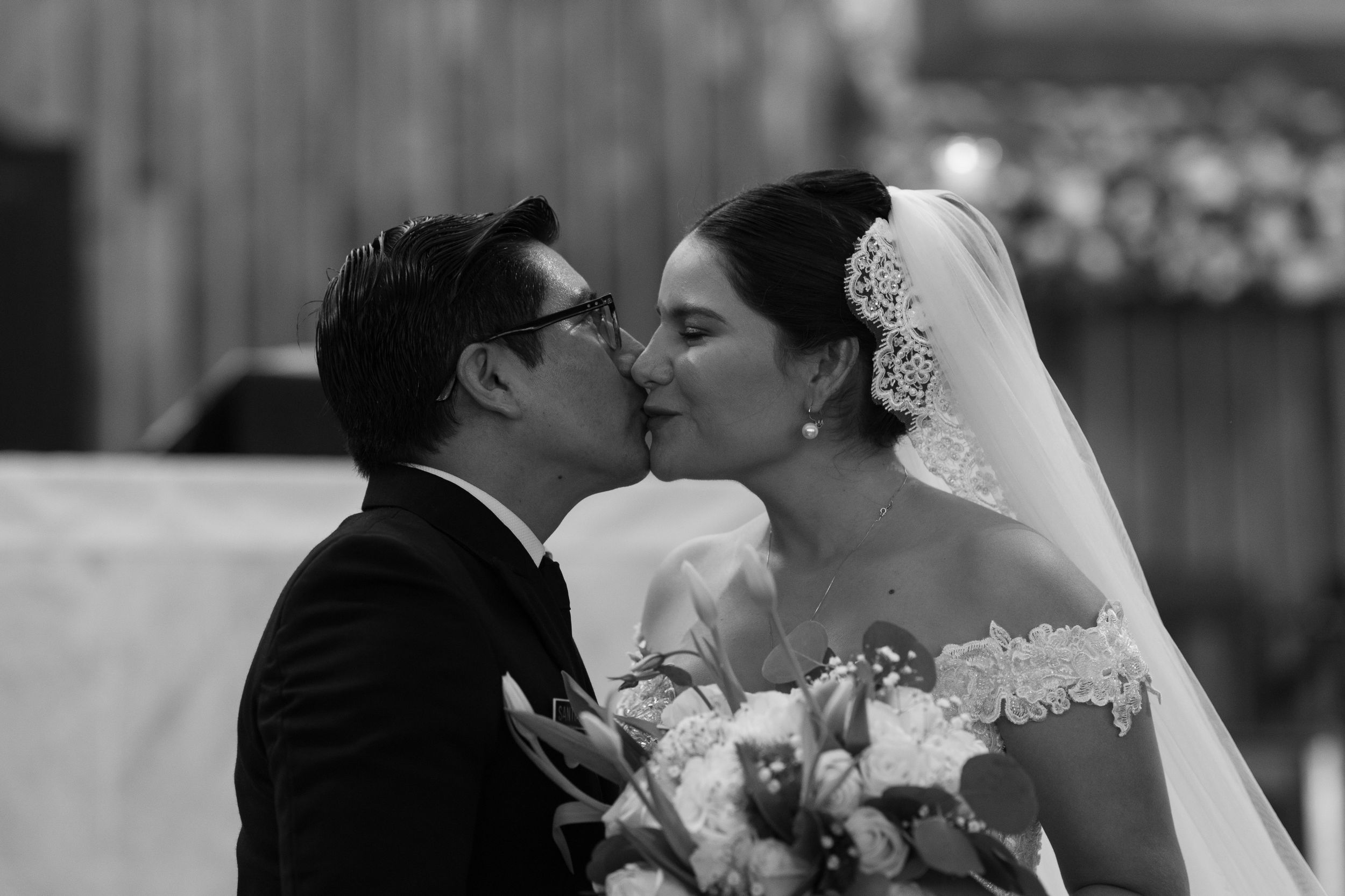 Black and white photo of a bride and groom sharing their first kiss at the altar during their wedding ceremony.