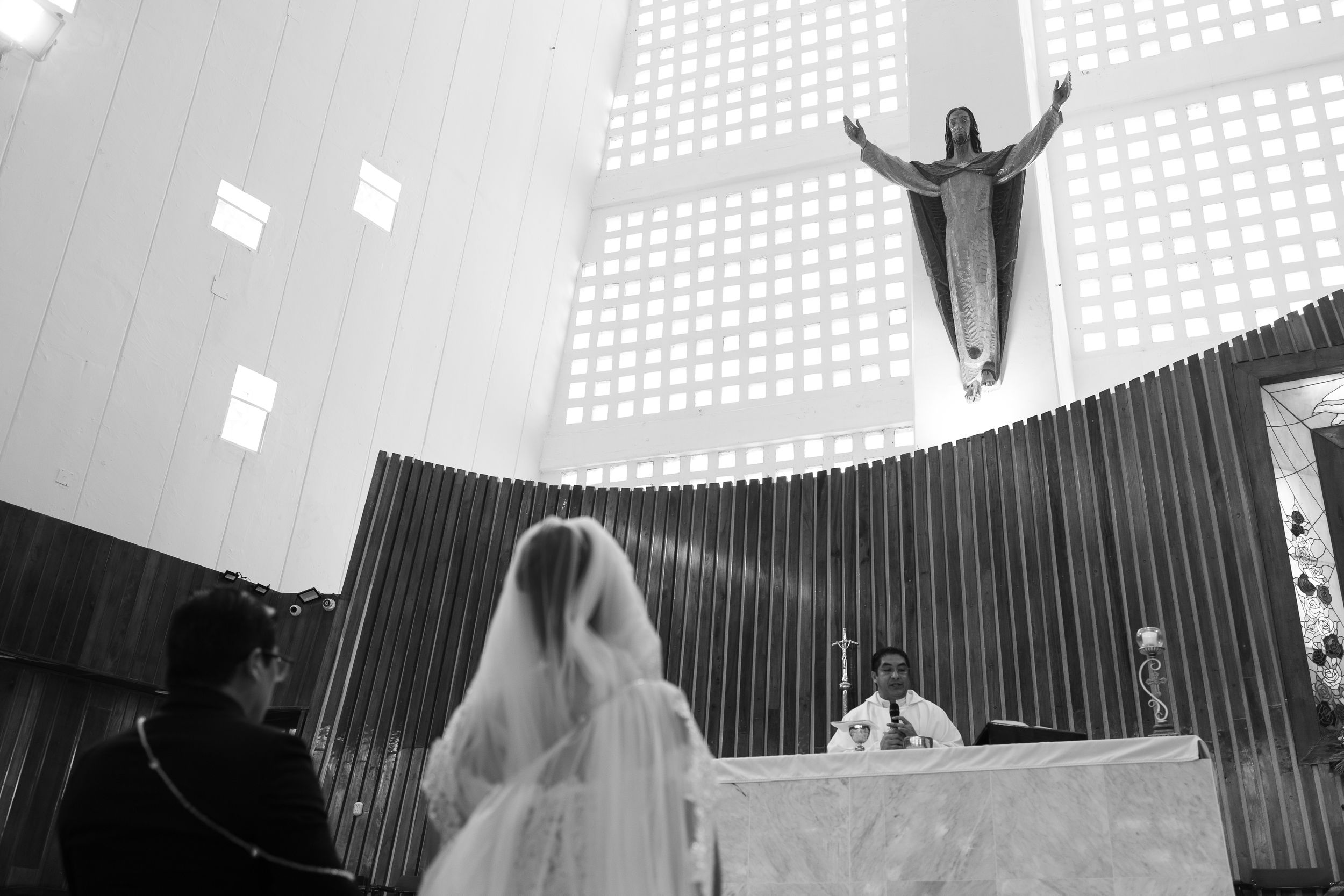 Black and white photo of a bride and groom at a Catholic church altar with a Jesus statue above.